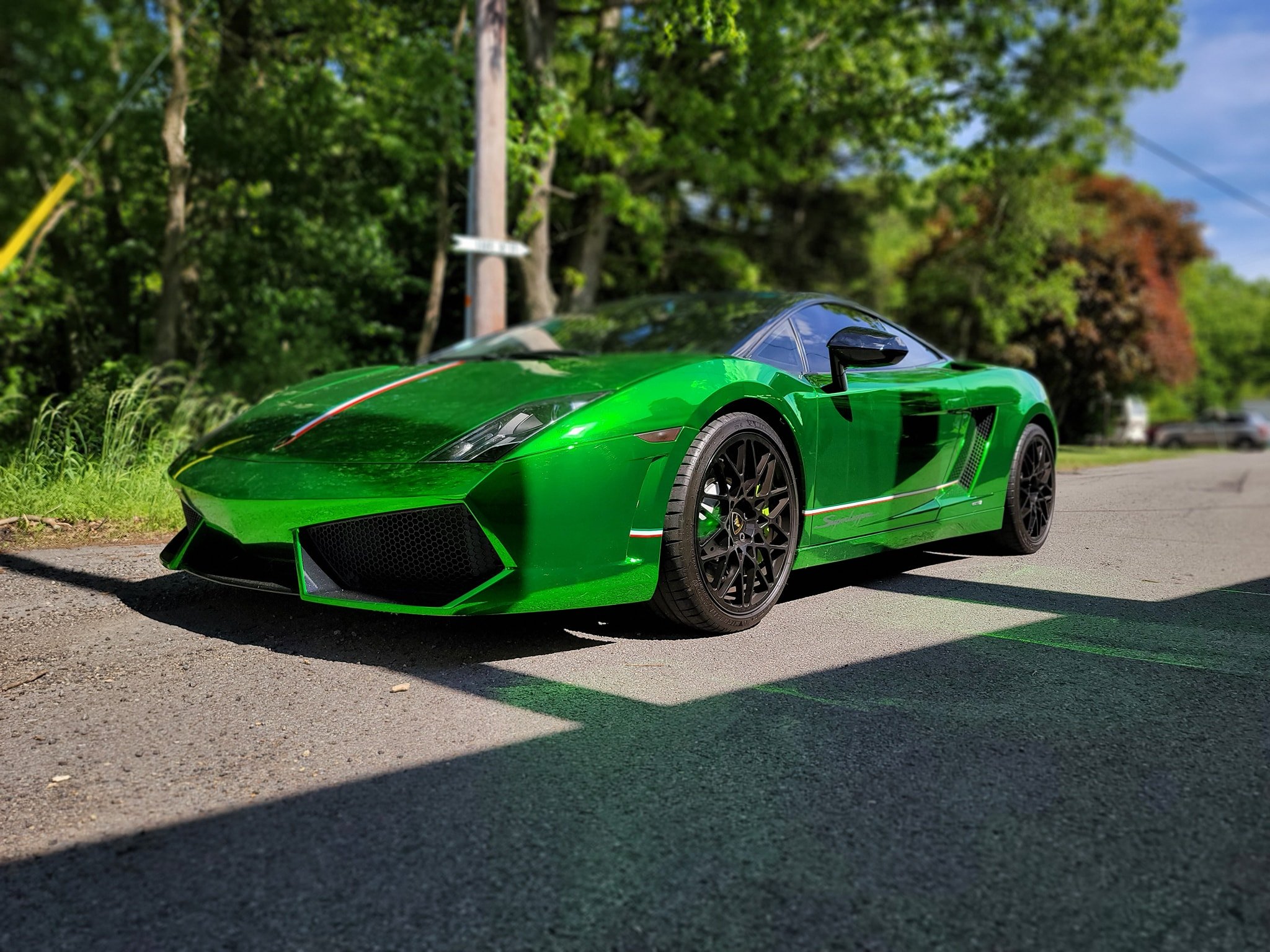 Green sports car parked on the side of the road with trees in the background.