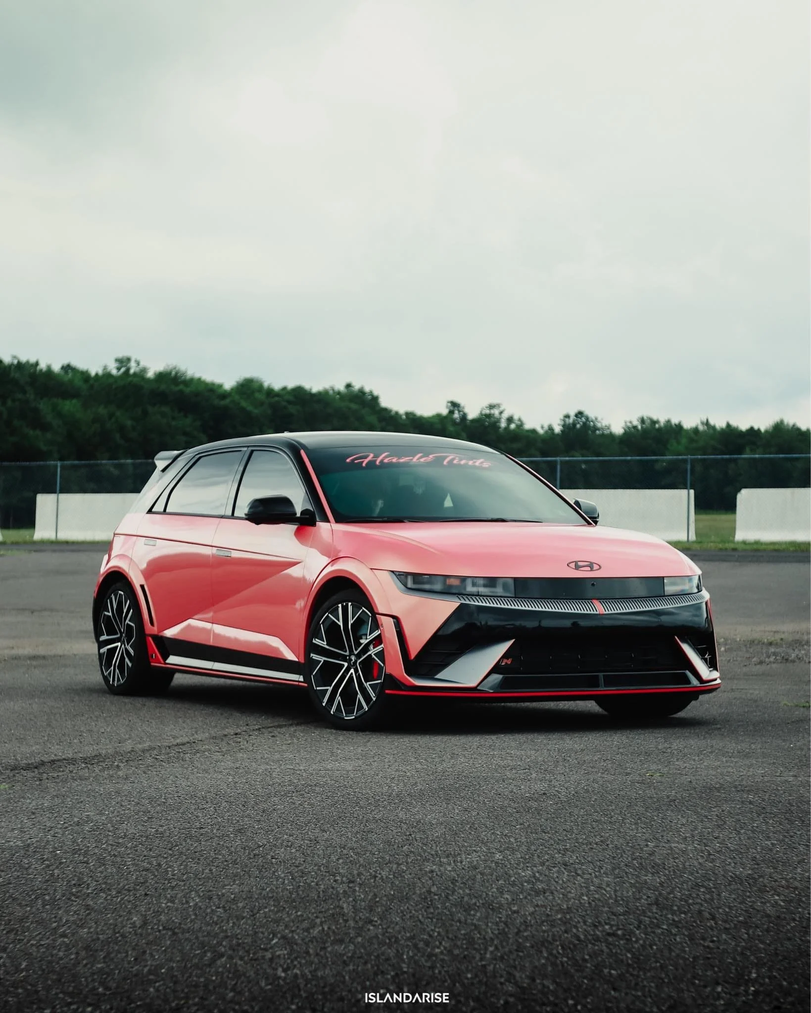 A red and black Hyundai electric concept car parked on an empty road with trees and a fence in the background.