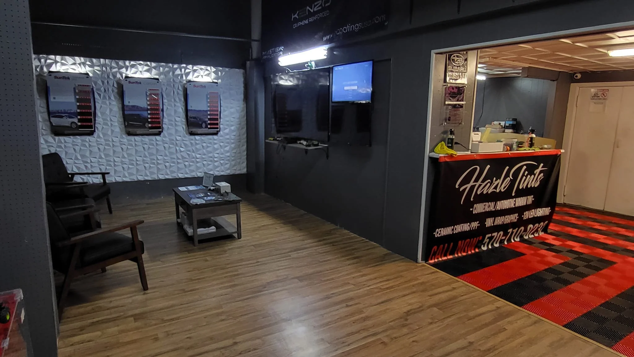 Indoor waiting area with black chairs and a small table, wall-mounted display screens, and a counter with a sign reading "Haze Tints."