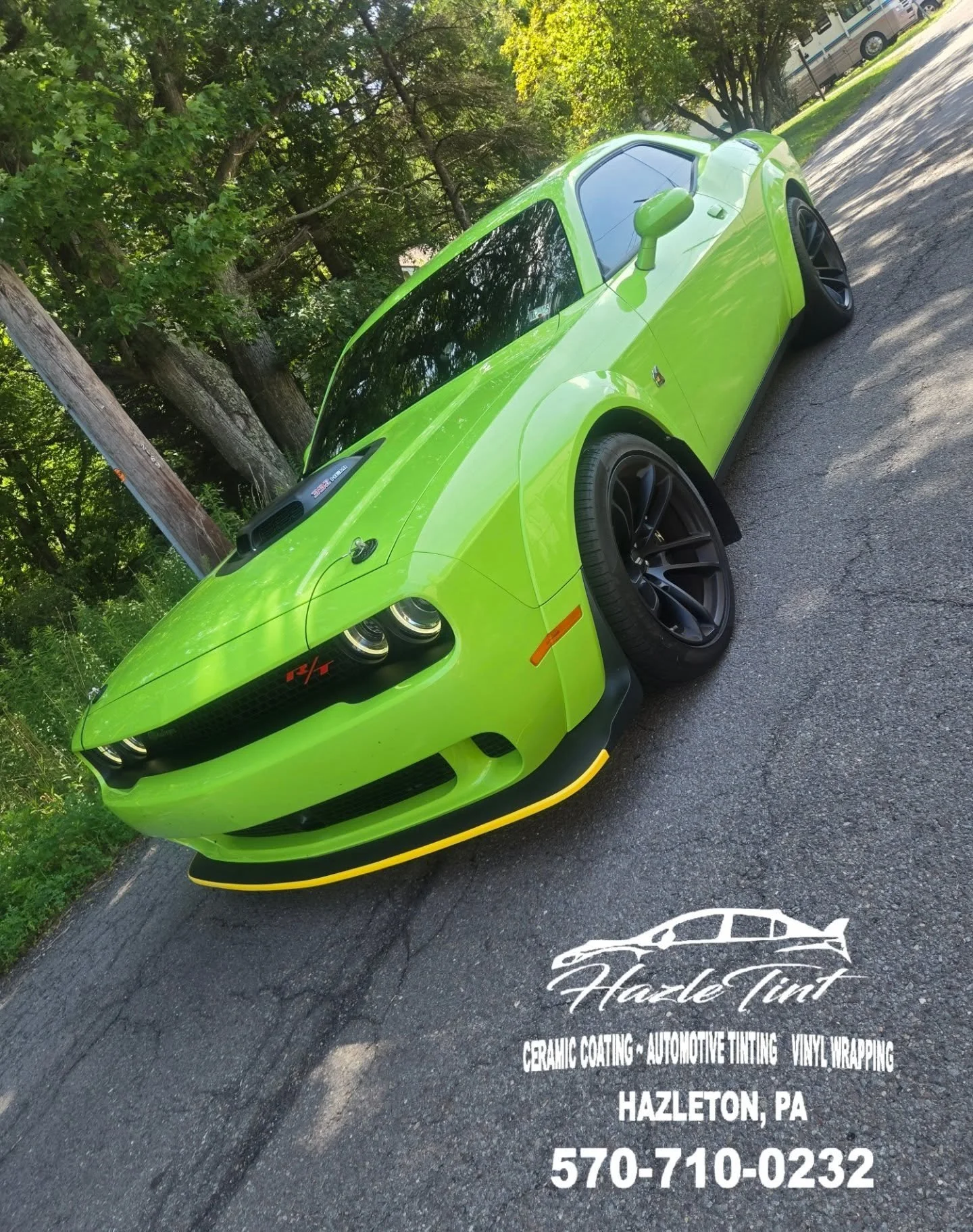 Bright green Dodge Challenger parked on asphalt, front view showing black wheels, tinted windows, and a black hood scoop, with trees in the background.