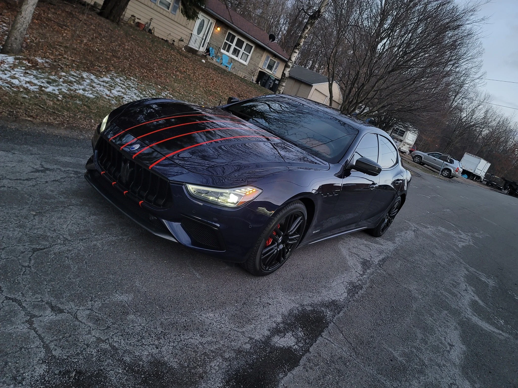 A black luxury sports car with red racing stripes parked on a gravel lot.