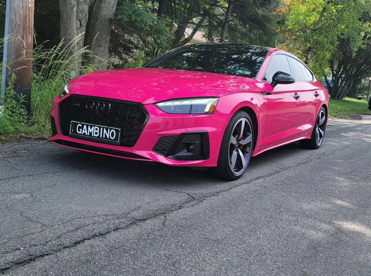 A vibrant pink Audi sedan parked on a street with green trees and grass in the background.