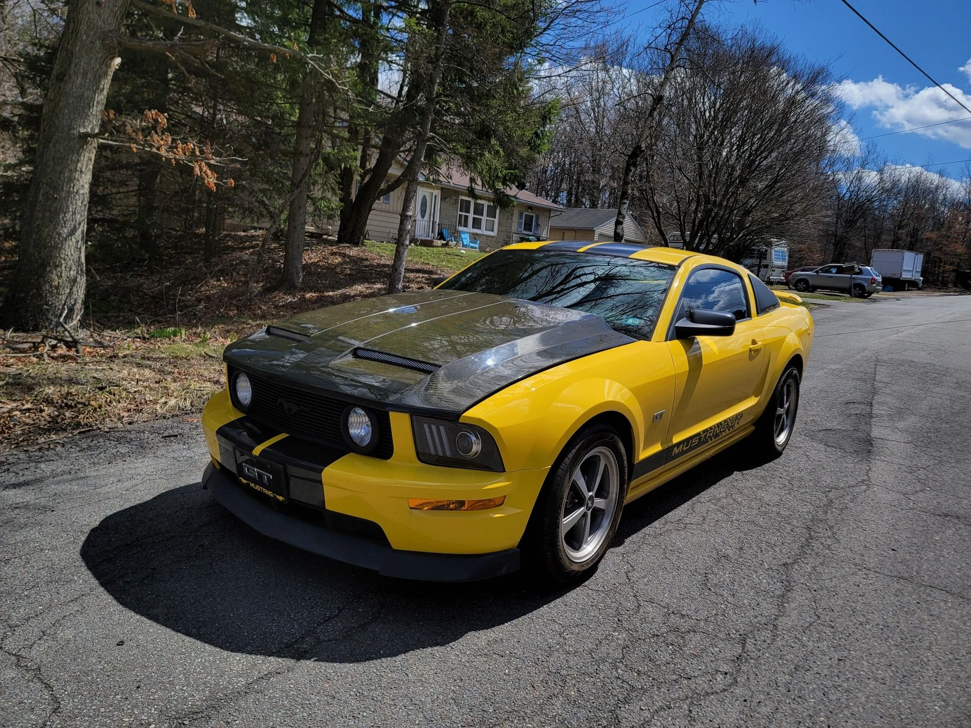 Yellow Ford Mustang GT with black hood and black racing stripes parked on a residential street.