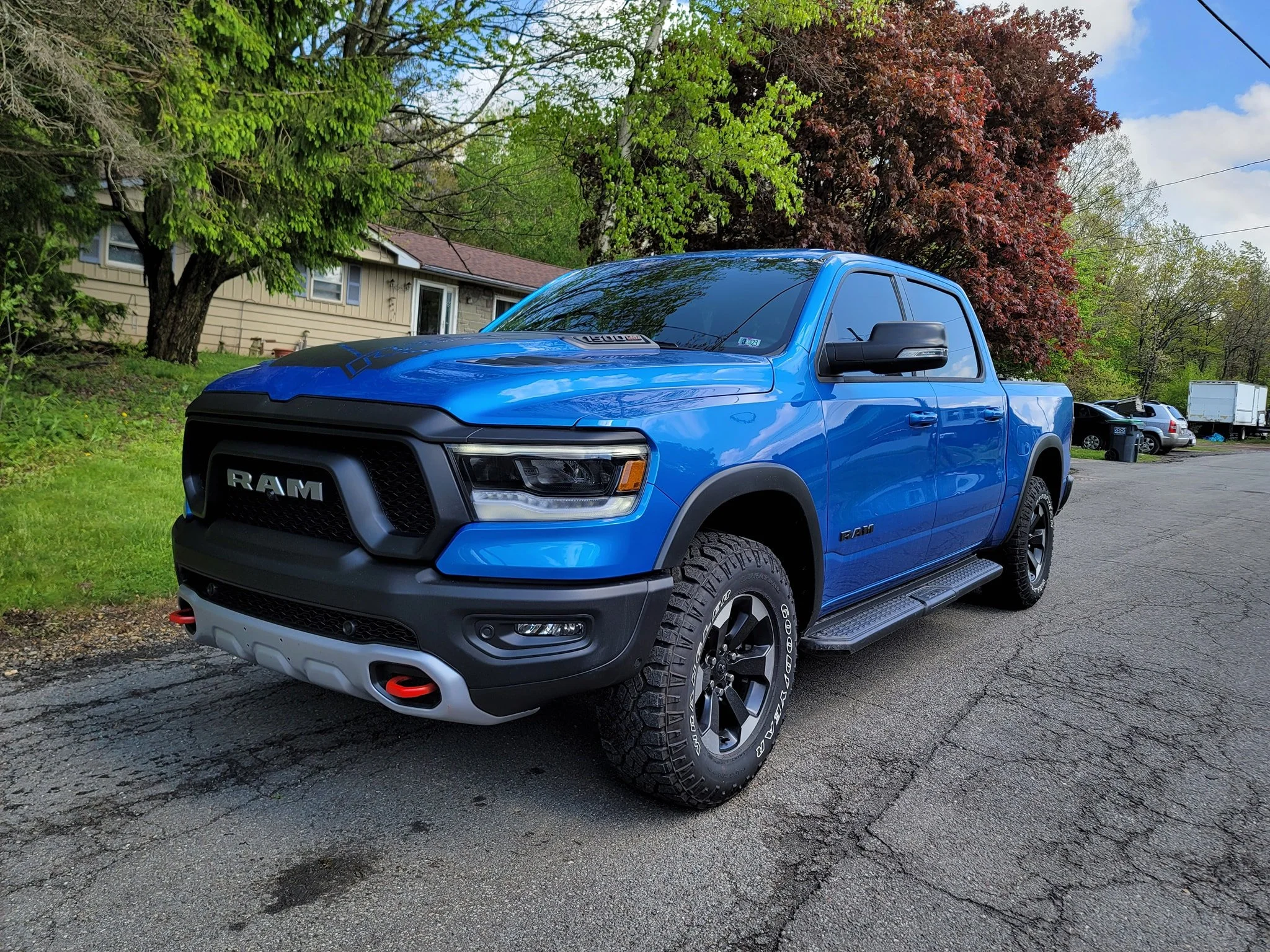 Blue RAM pickup truck parked on a driveway with trees and a house in the background.