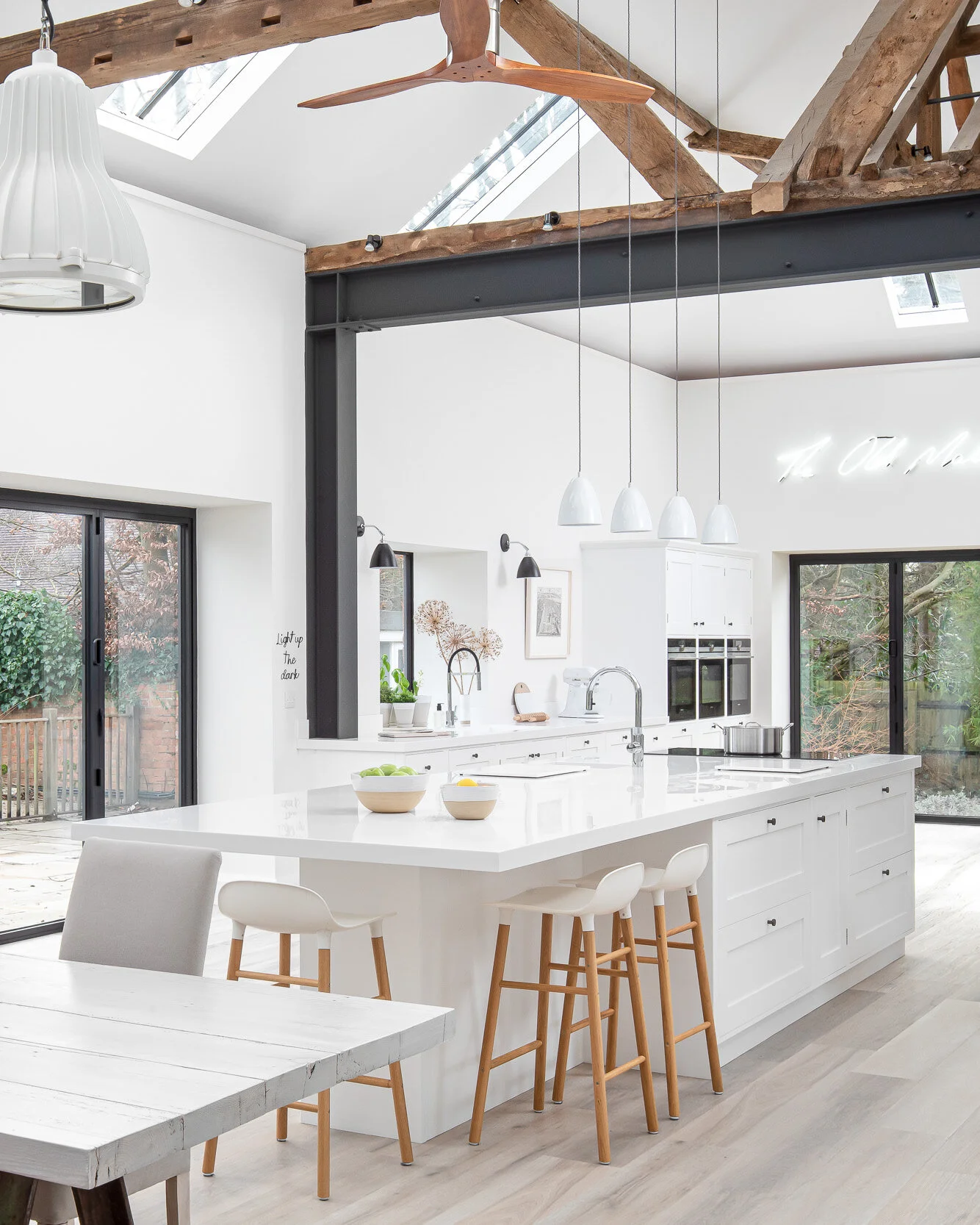 Modern kitchen with white cabinetry, large island with bar stools, overhead wooden beams, pendant lighting, and sliding glass doors leading to a patio.