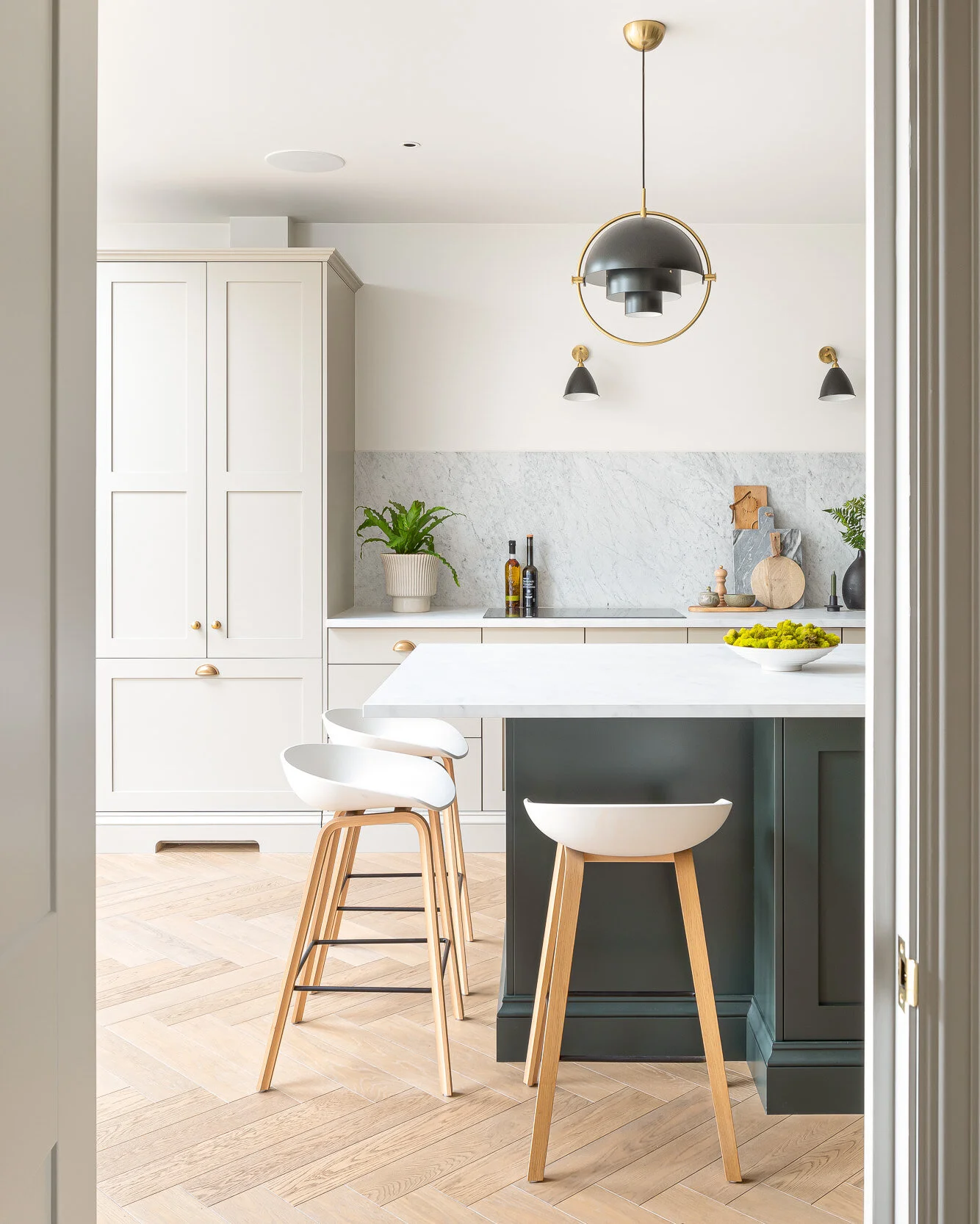 Modern kitchen with wooden floors, a marble countertop island with white bar stools, pendant lighting, and minimalist decor.