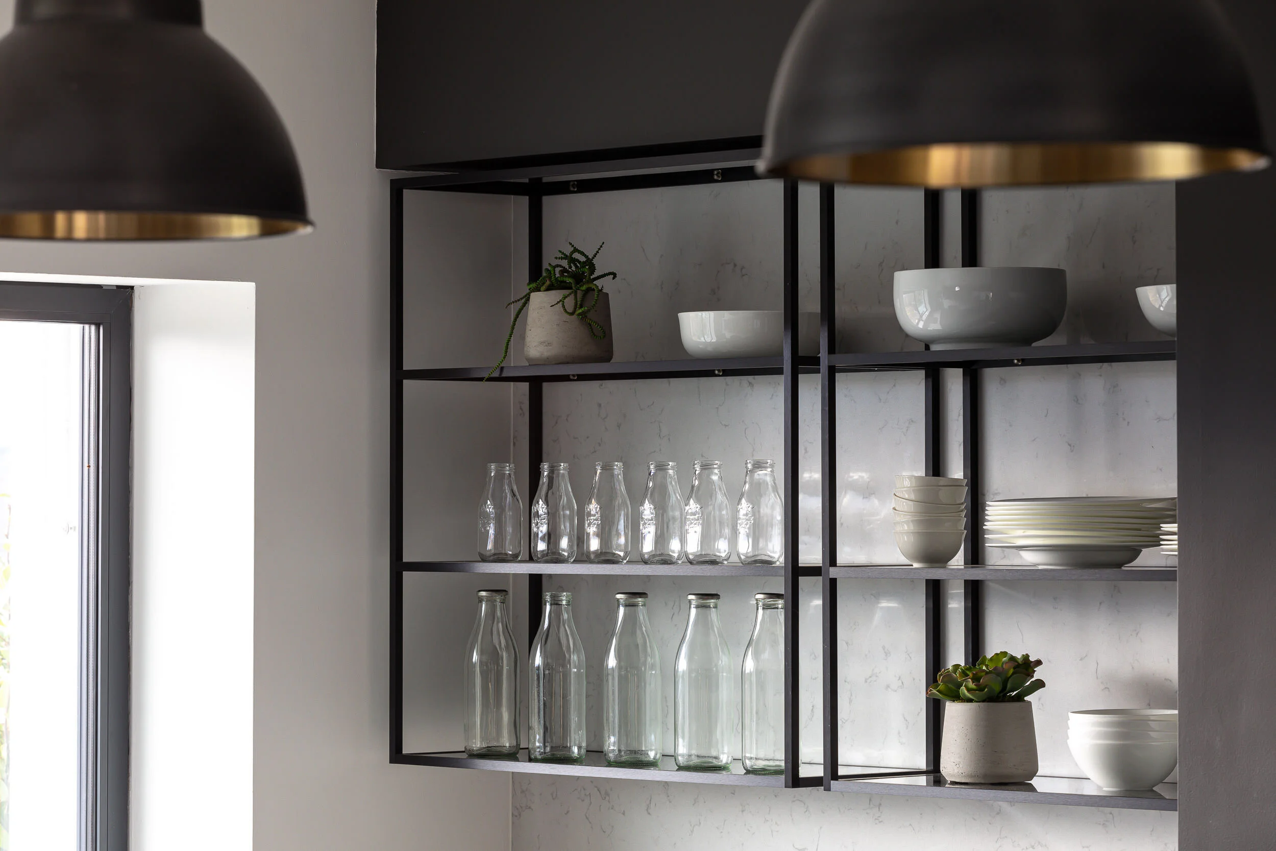 Modern kitchen shelves with glass bottles, white dishes, and potted plants.