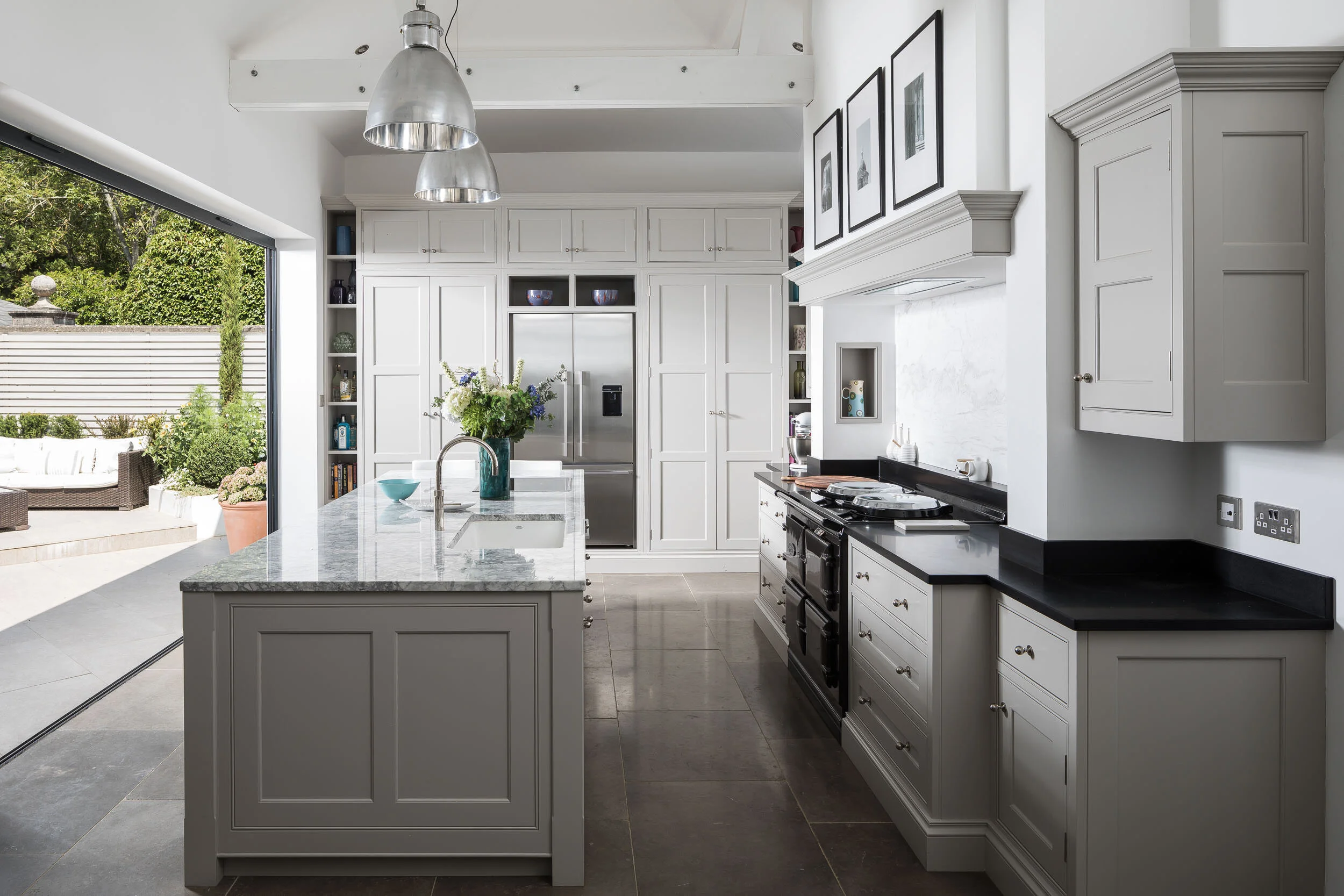 Modern kitchen with marble island, stainless steel appliances, black countertops, pendant lights, and open patio doors.