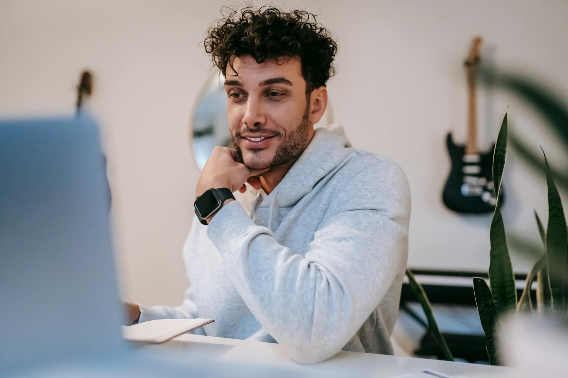 Man met krullend haar zit aan zijn bureau, kijkt naar een laptop naar een uitlegvideo van zijn Squarespace website gemaakt door Made by Anouk Square Space expert van Nederland. 