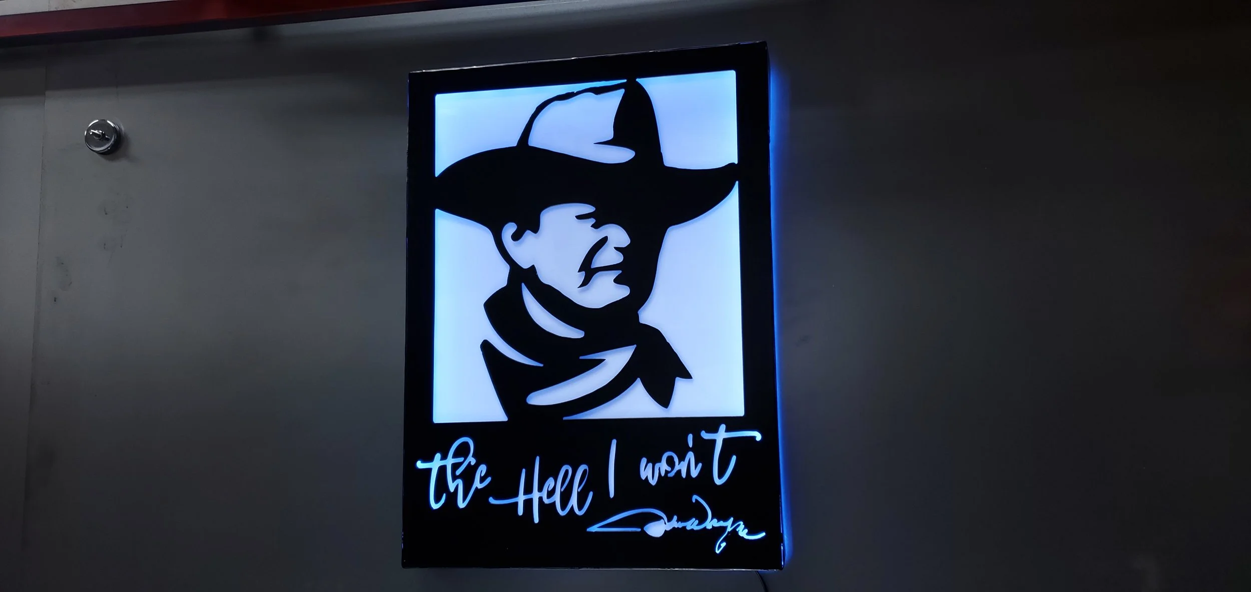 Illuminated sign featuring a silhouette of a man wearing a cowboy hat and bandana, with the text "the Hell I won't" written below.