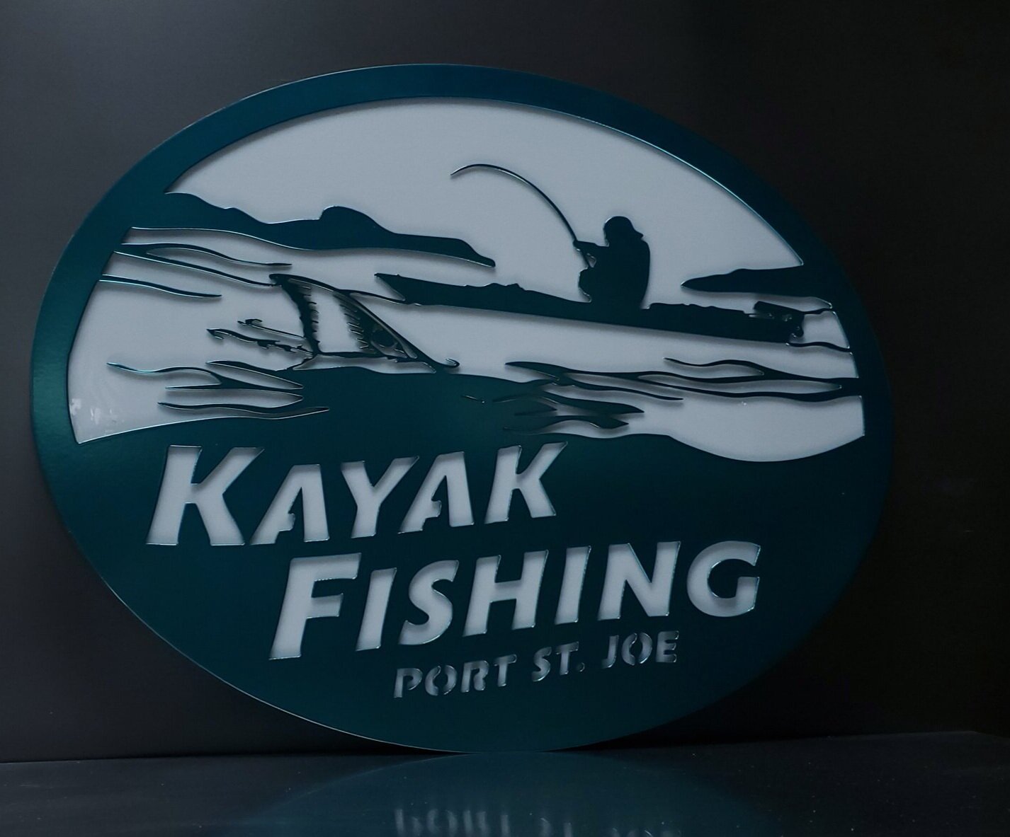 Round sign with silhouette of a person fishing from a boat on water, with the text "KAYAK FISHING PORT ST. JOE"
