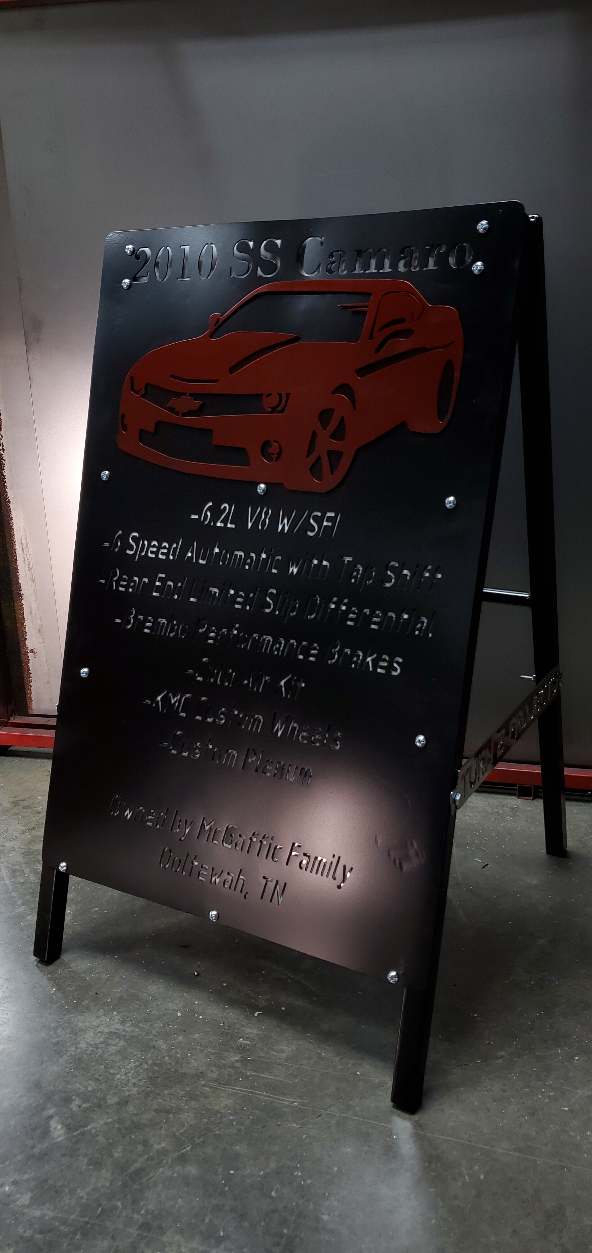 A black metal A-frame sign featuring details about a 2010 Chevrolet Camaro, including a red outline of the car and specifications such as a 6.2L V8 engine, 6-speed automatic transmission, and Brembo brakes, located in Tennessee.