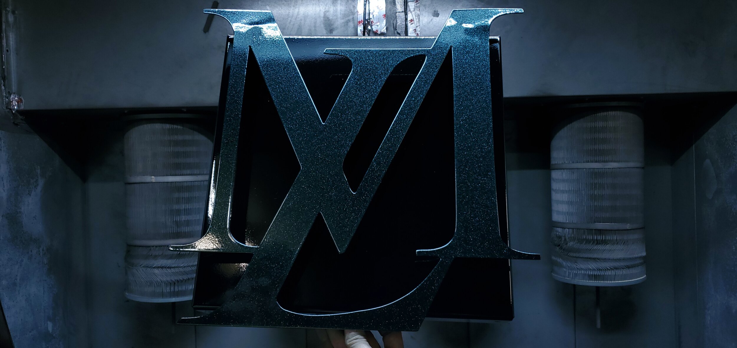 A large metallic WWE logo on a black background, with two rolls of clear plastic sleeves in the background.