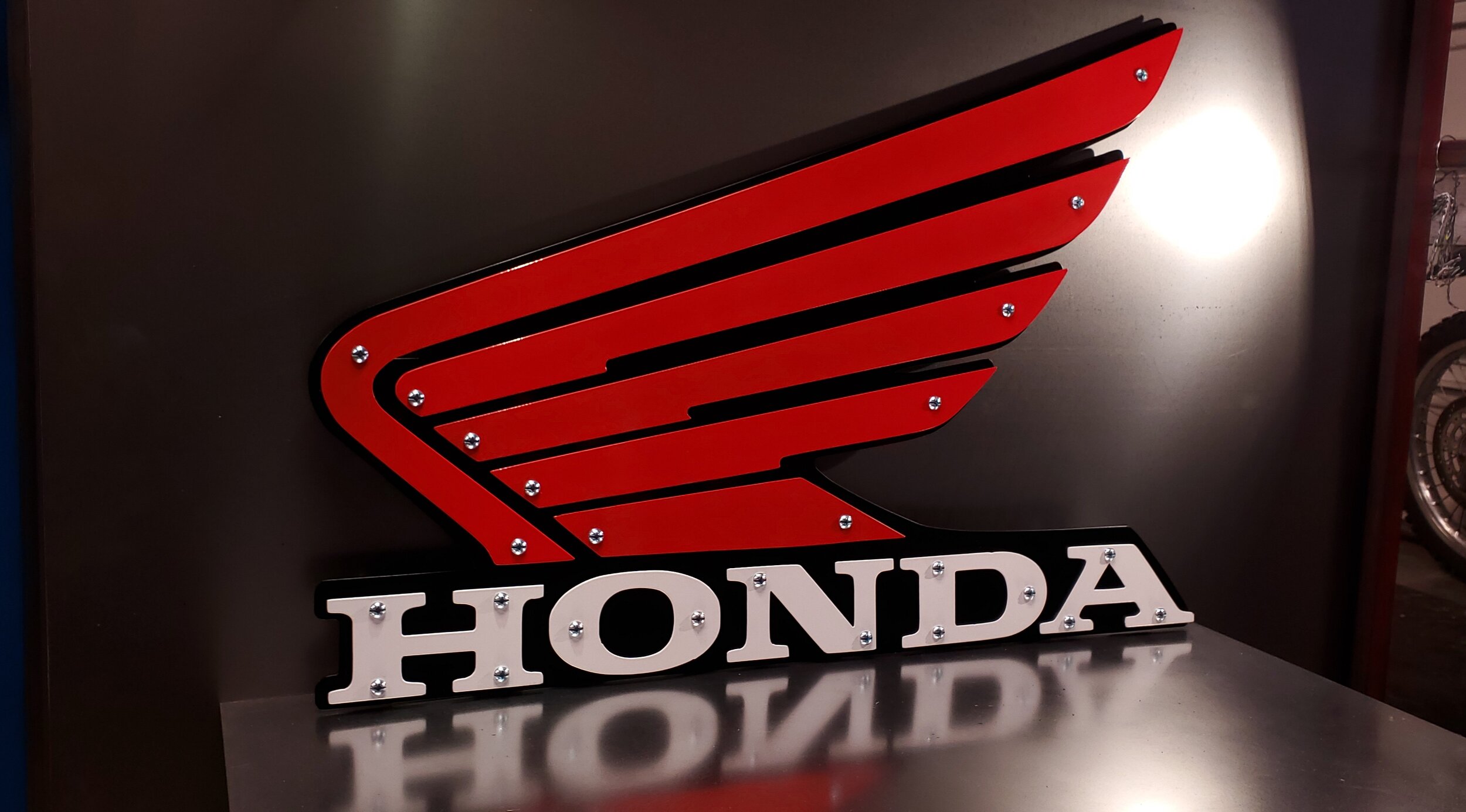 A sign of the Honda logo with red stylized wings and white letters spelling 'Honda' on a black background.