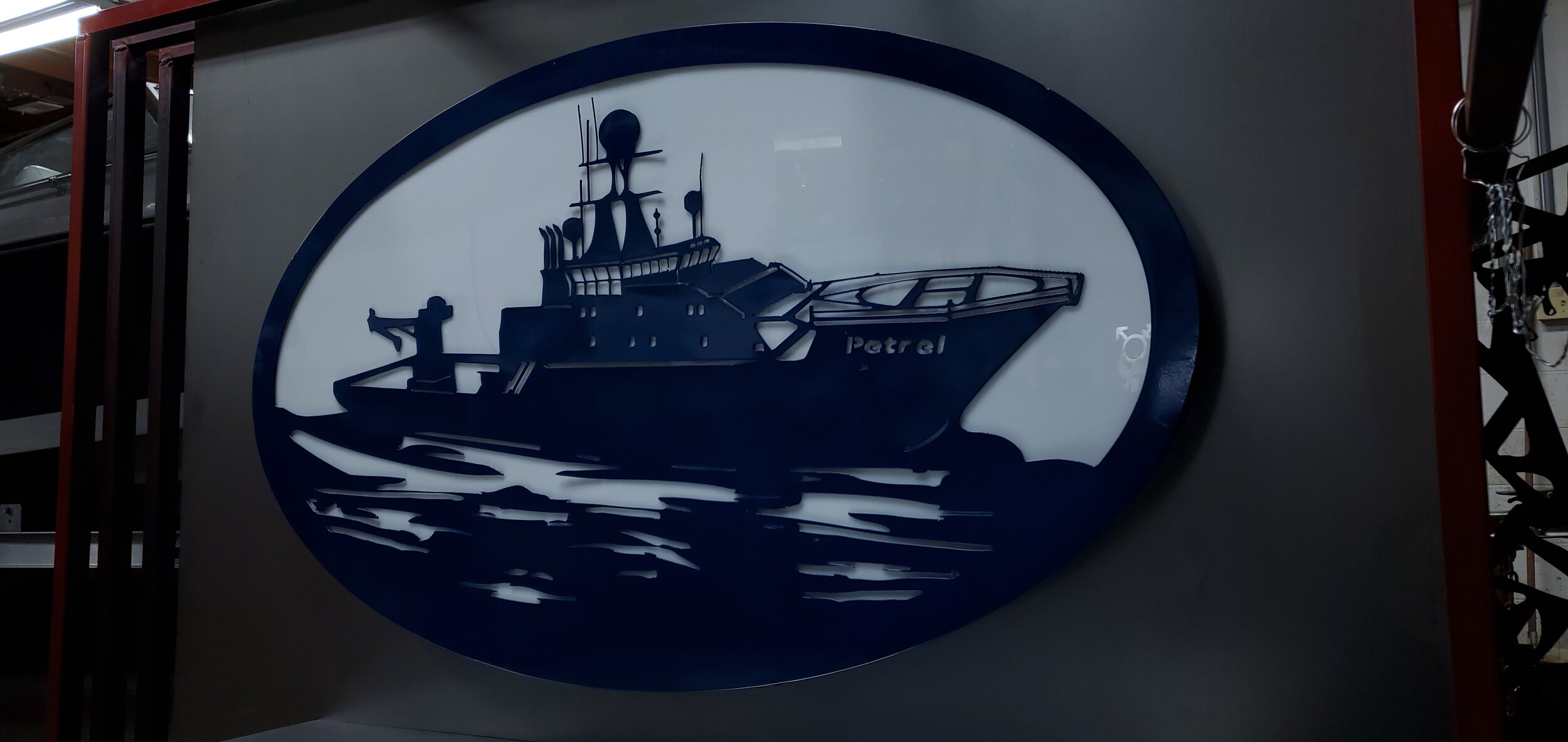 Metal sign with a silhouette of a boat labeled "Petrel" on water.