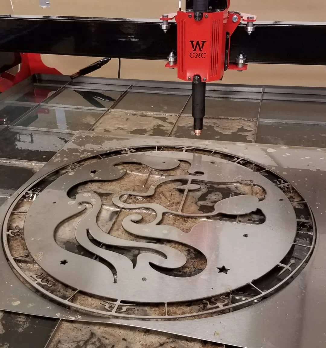 A CNC laser cutter engraving a design on a metal clock face with Roman numerals.
