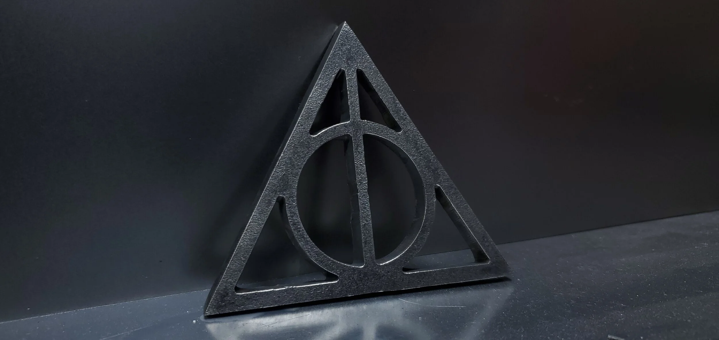 A black, metal triangular emblem with a circle and lines inside, placed on a dark surface against a black background.