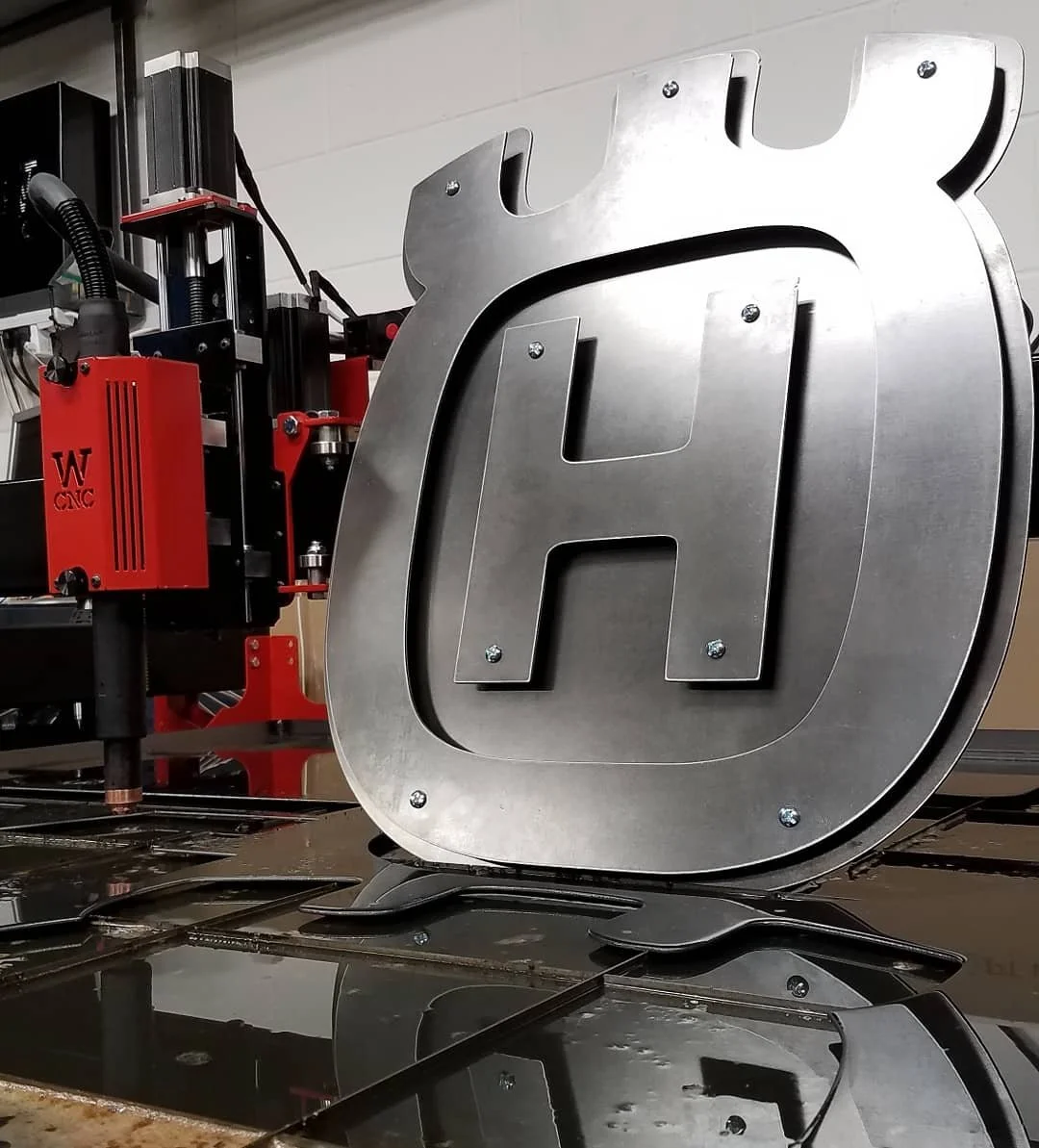 A metal sign with a large letter 'H' attached to a CNC machine.