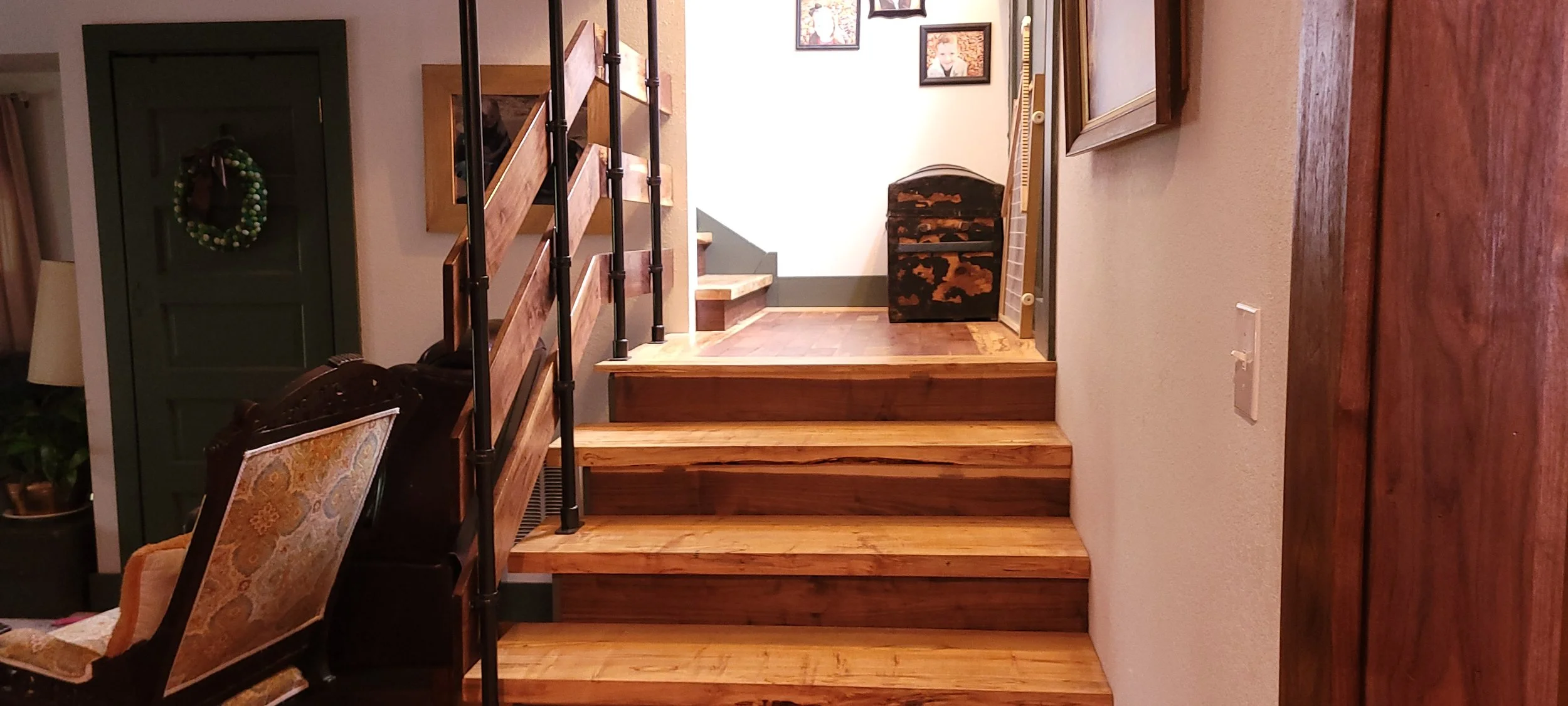 Wooden stairs leading to an upper floor in a home, with a black and brown patterned storage chest at the top and framed photos on the wall.
