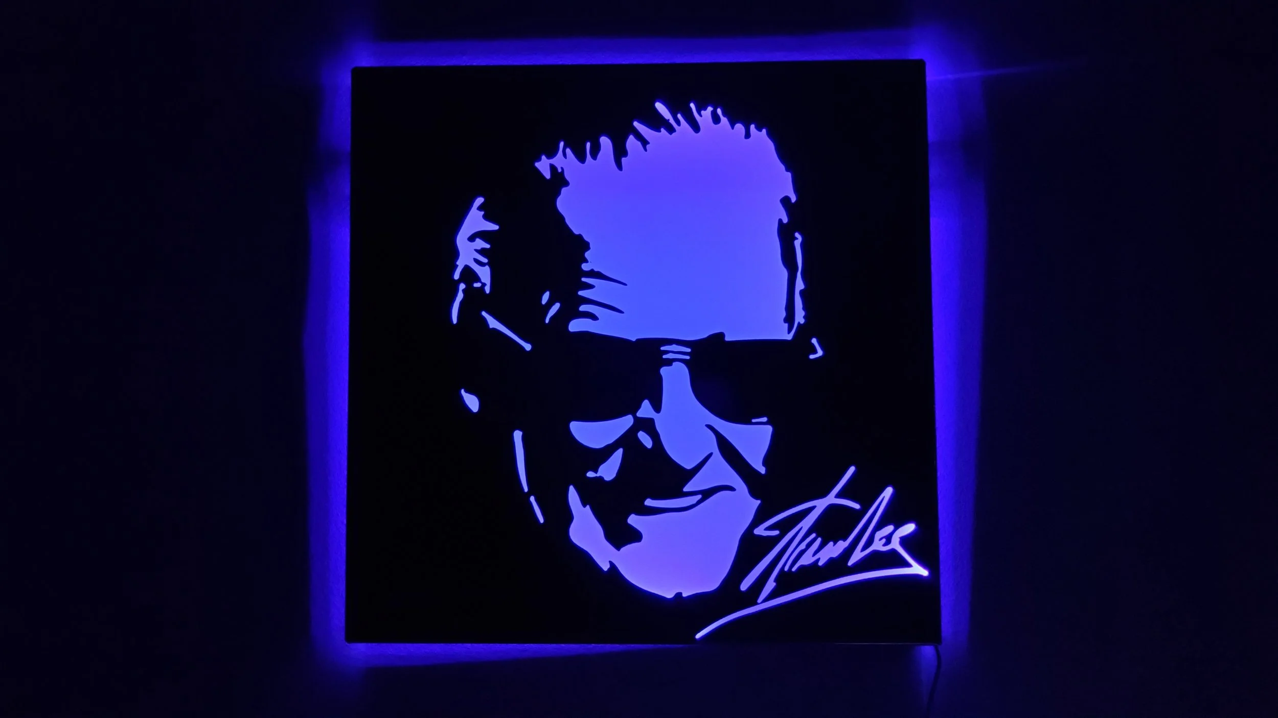 Silhouette of a person with spiky hair and sunglasses, illuminated by blue light, with a signature at the bottom right.