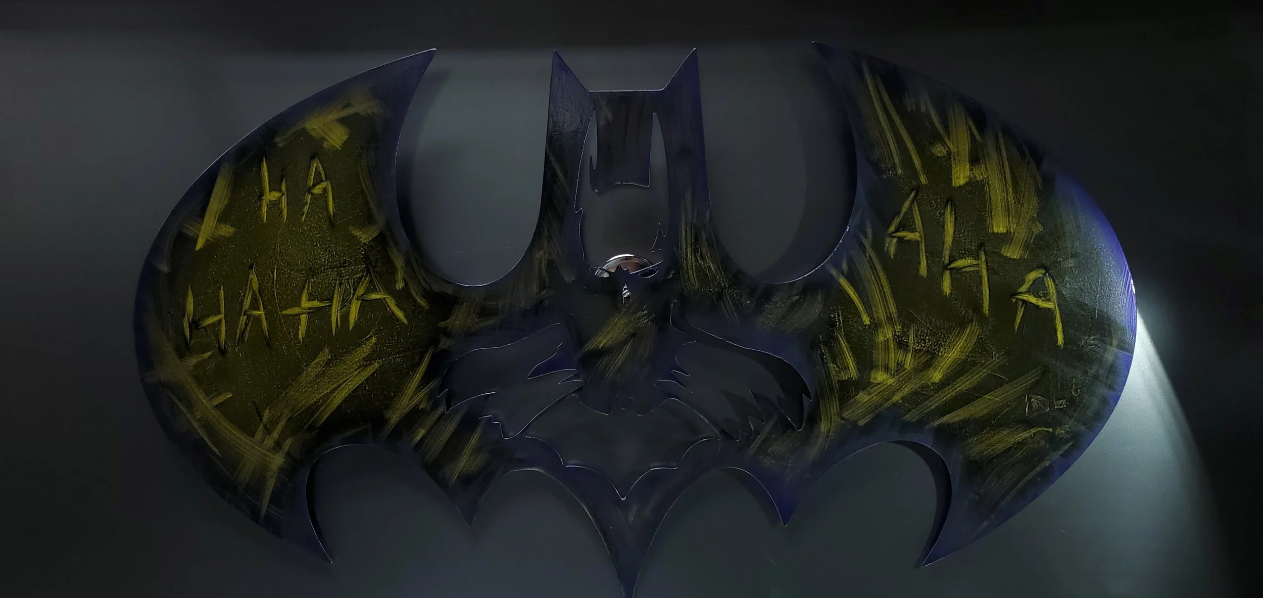 Dark Batman logo with yellow graffiti-style markings and the words 'HA HA' written multiple times.