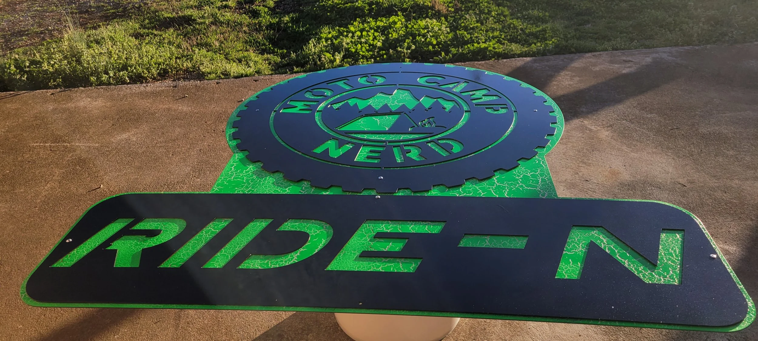 A manhole cover with the words 'Mountain & NERD' and a logo featuring mountain peaks, against a sidewalk background. Made by Turn 2 Customz