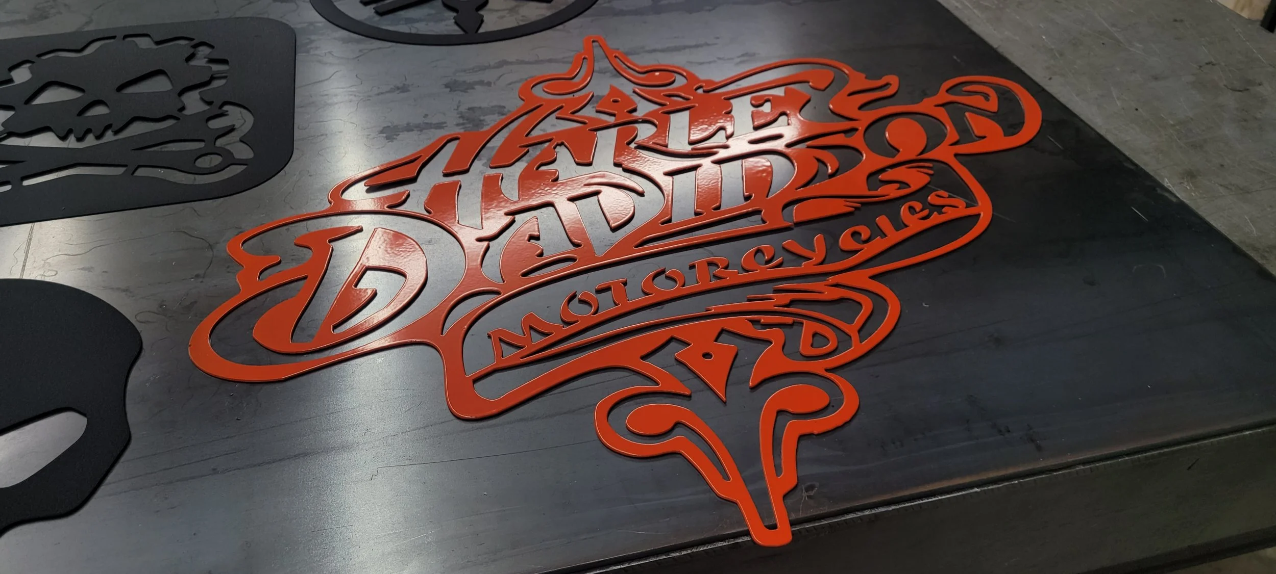 A decorative sign in orange metal with the words 'Viet Fashions' and 'Houston, TX' outlined in a stylized font, lying flat on a black surface.