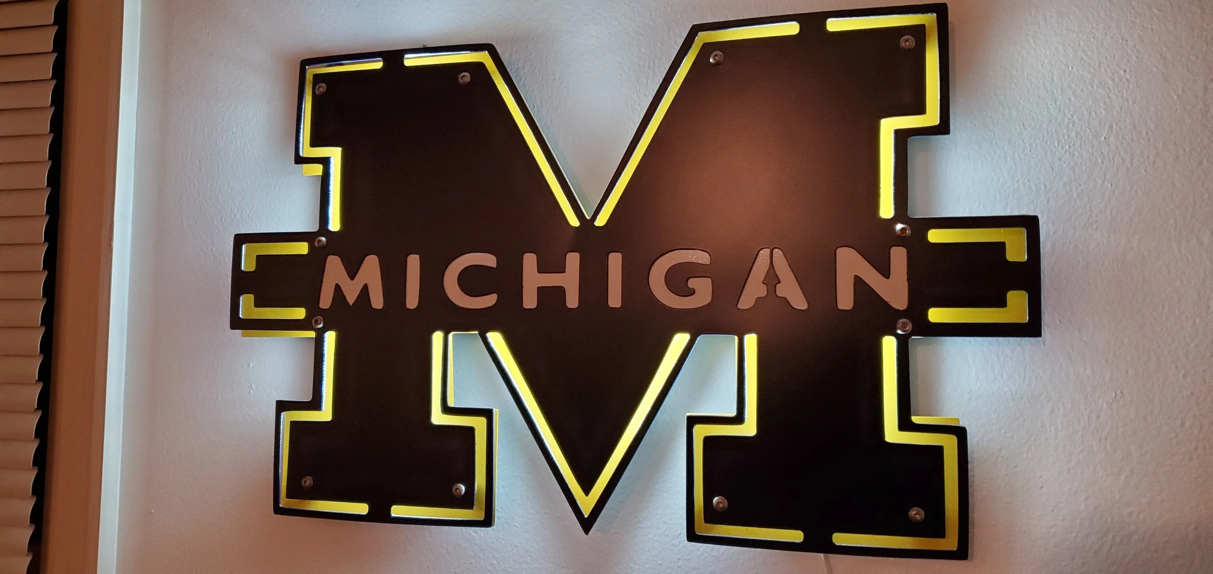 Neon sign of the word 'LOVE' with 'MICHIGAN' written across the middle of the 'O' in yellow and pink letters, mounted on a wall.