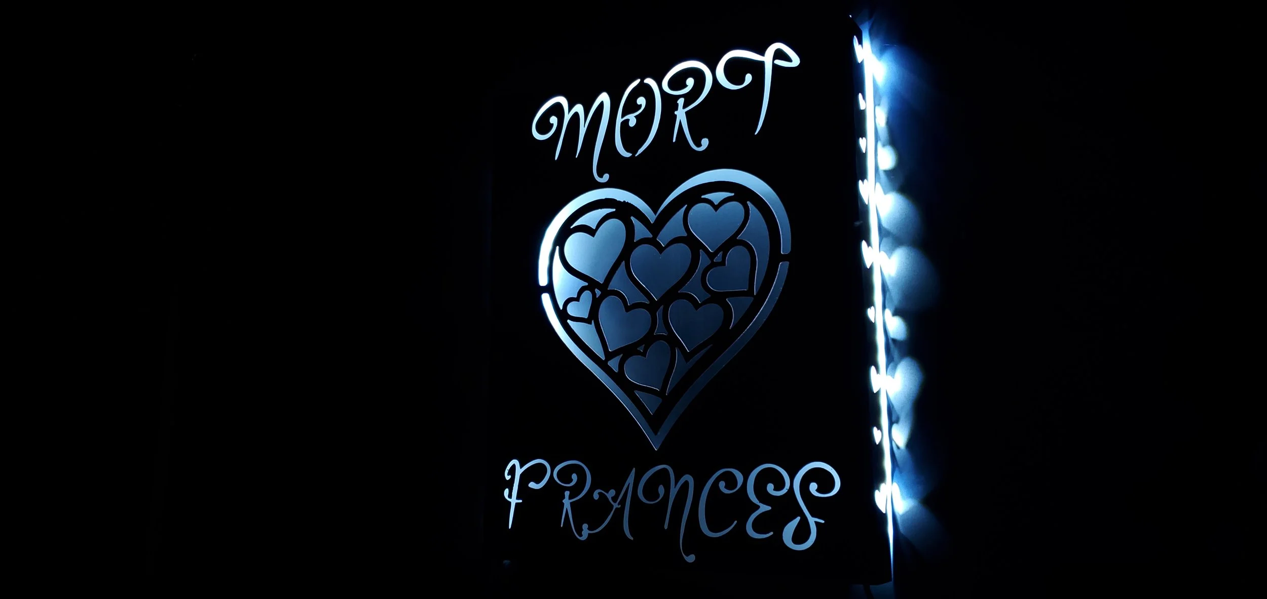 Neon sign with the words "MORT PRINCES" and a heart-shaped design filled with smaller hearts, illuminated in blue against a black background.