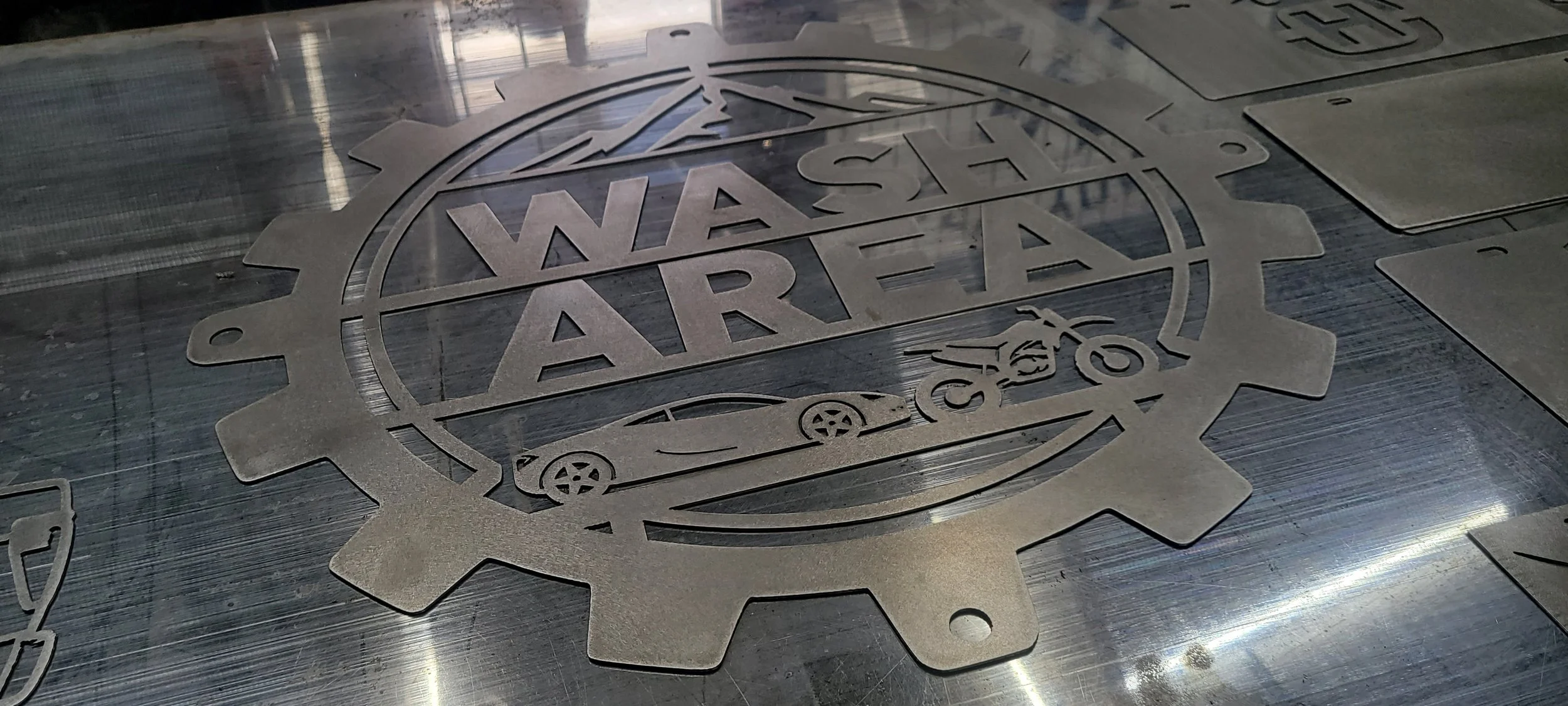Metal sign with the words 'WASH' and 'ART' separated by a skateboard graphic, surrounded by a gear-like border, placed on a metallic surface. Made by Turn 2 Customz