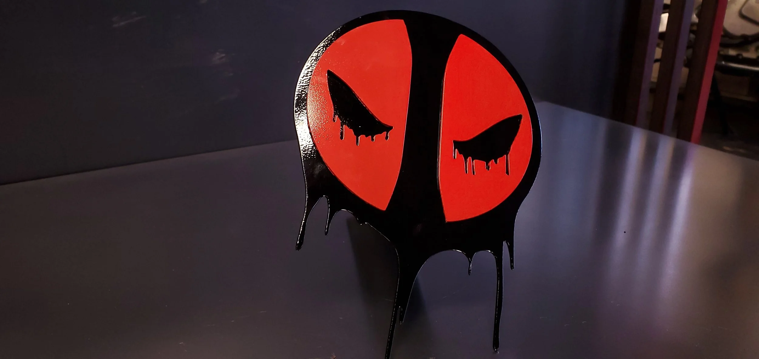 Black and red Halloween-themed decoration with dripping paint effect, featuring two stylized, dripping paint bats on a round background.