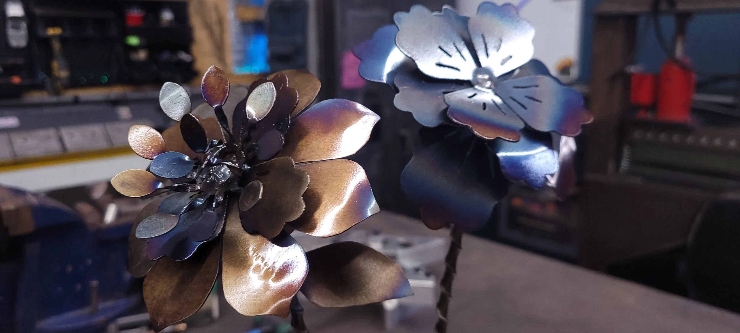 Close-up of metallic flower sculptures with a workshop in the background. Custom plasma cut metal flowers fabricated by Turn 2 Customz in Tellico Plains Tennessee