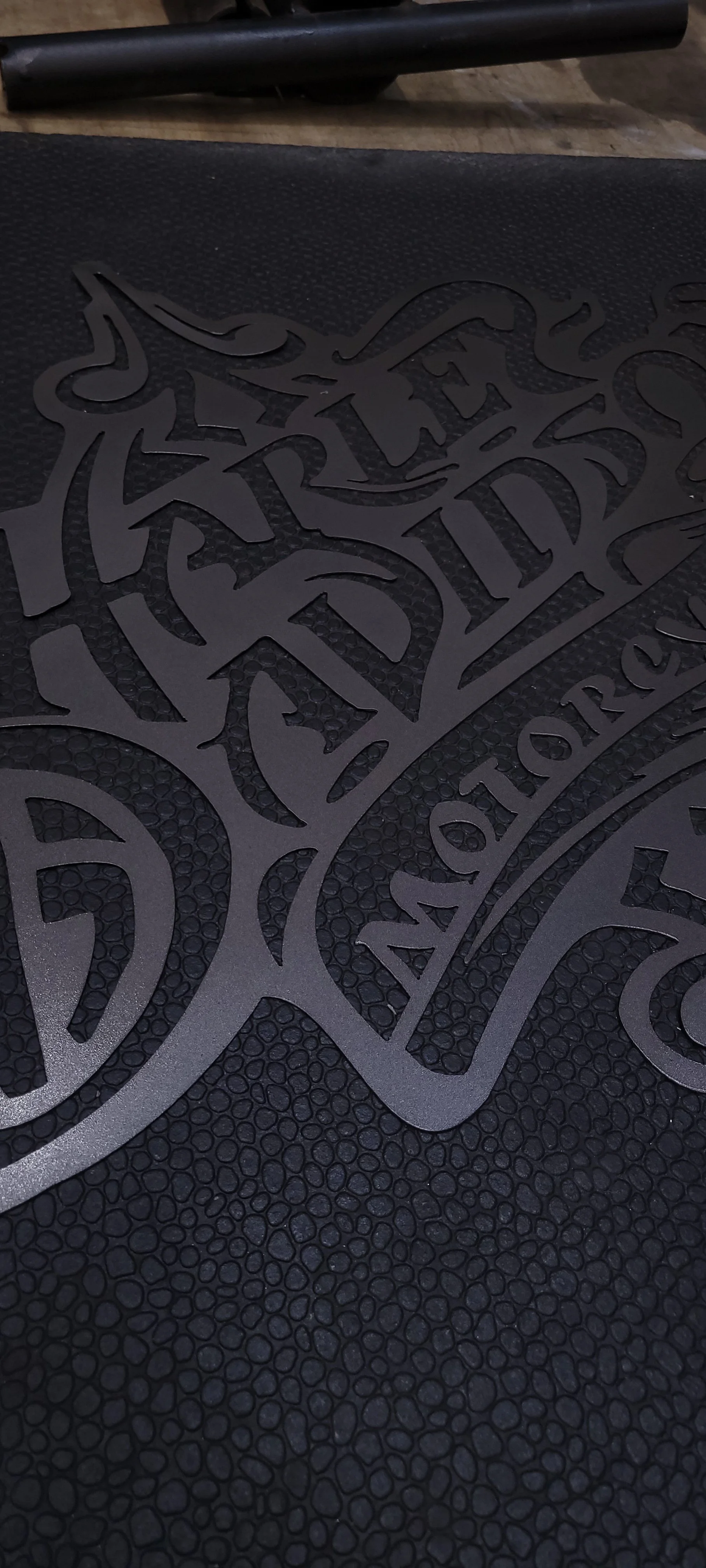 Close-up of a black surface with a decorative design and text that reads "AMERITRADE" on a textured background. Part of a dumbbell is visible in the background.