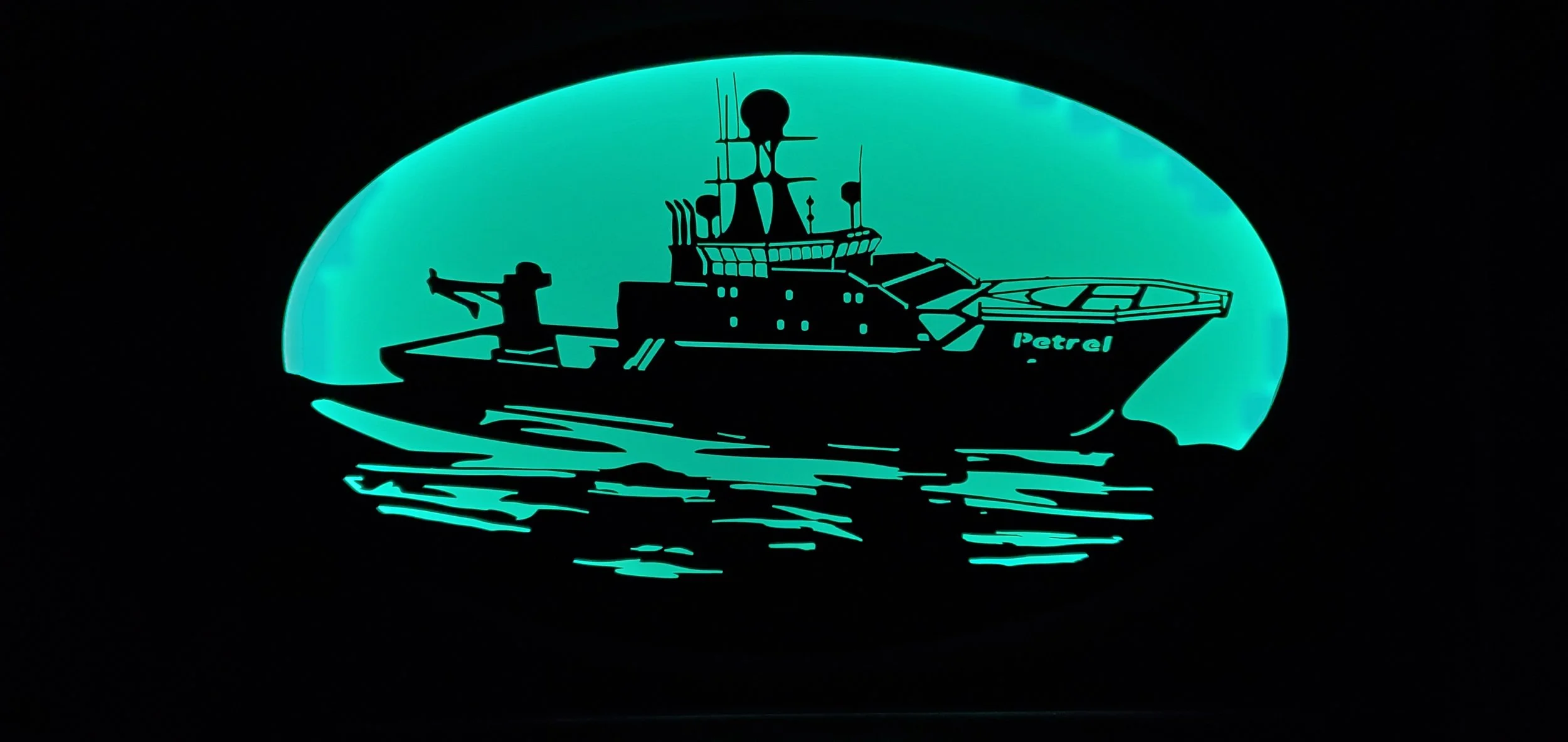 Silhouette of a boat named 'Petrel' illuminated against a glowing blue background, reflecting on water.