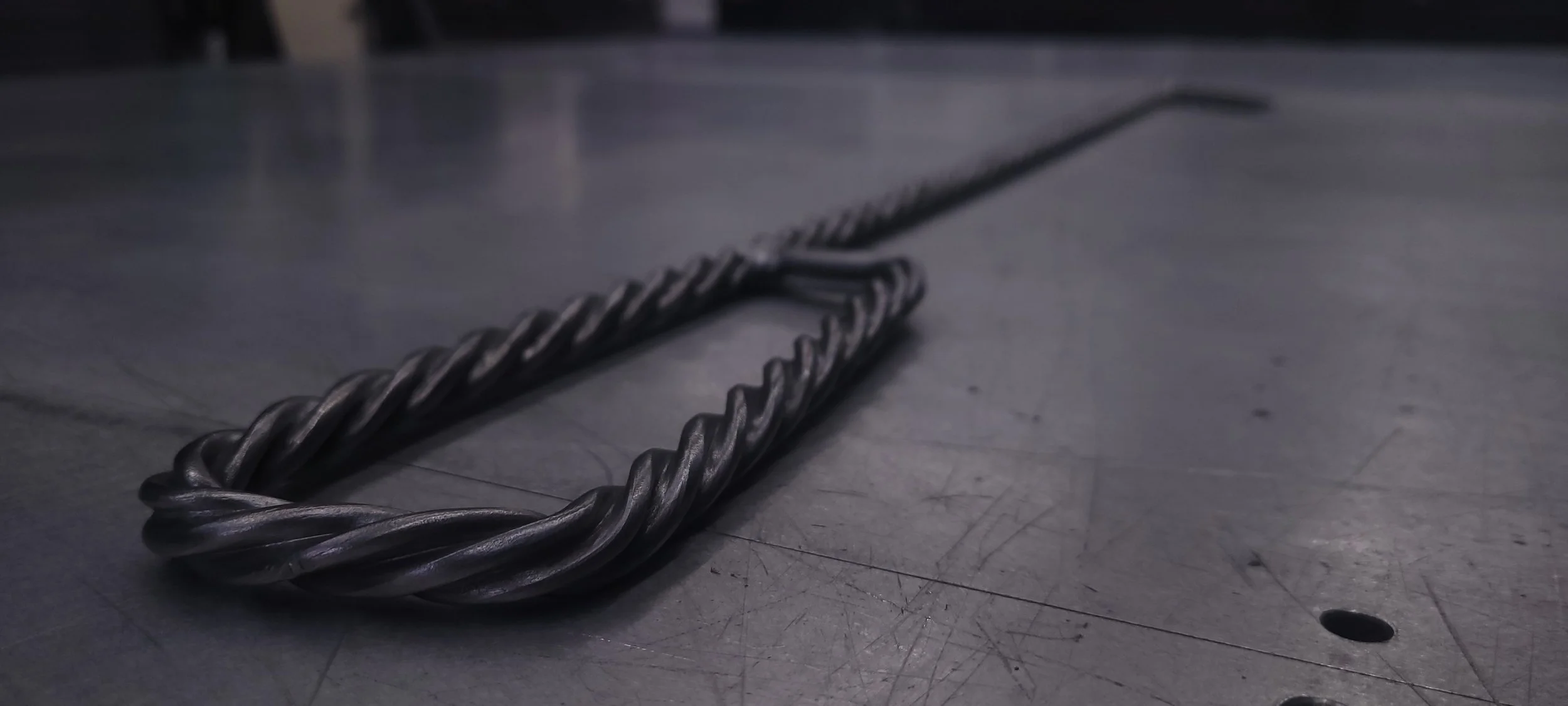 A metal twisted rebar wire on a gray, scratched metal surface.