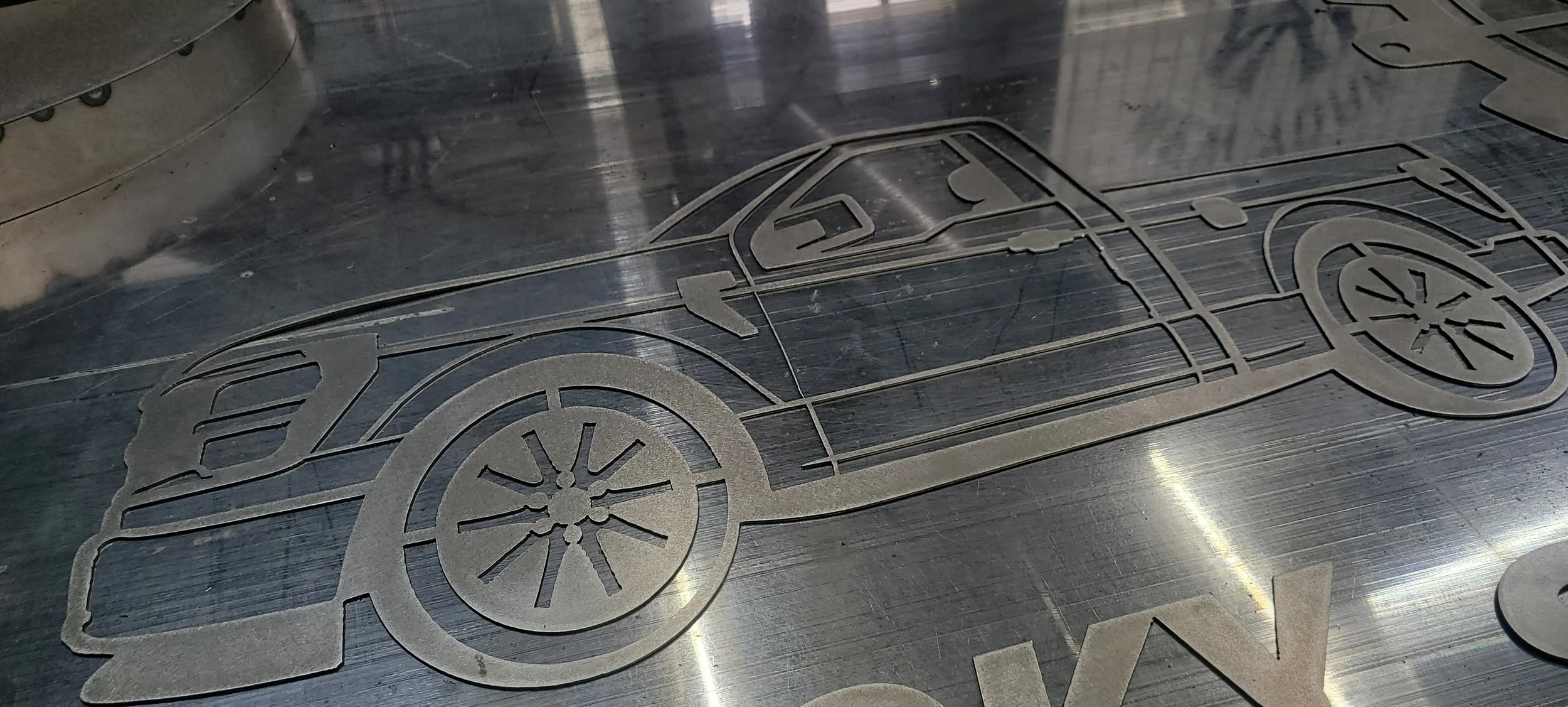 A metallic surface featuring an engraved outline of a vintage car, showcasing details like the wheels, body, and windows. Made by Turn 2 Customz