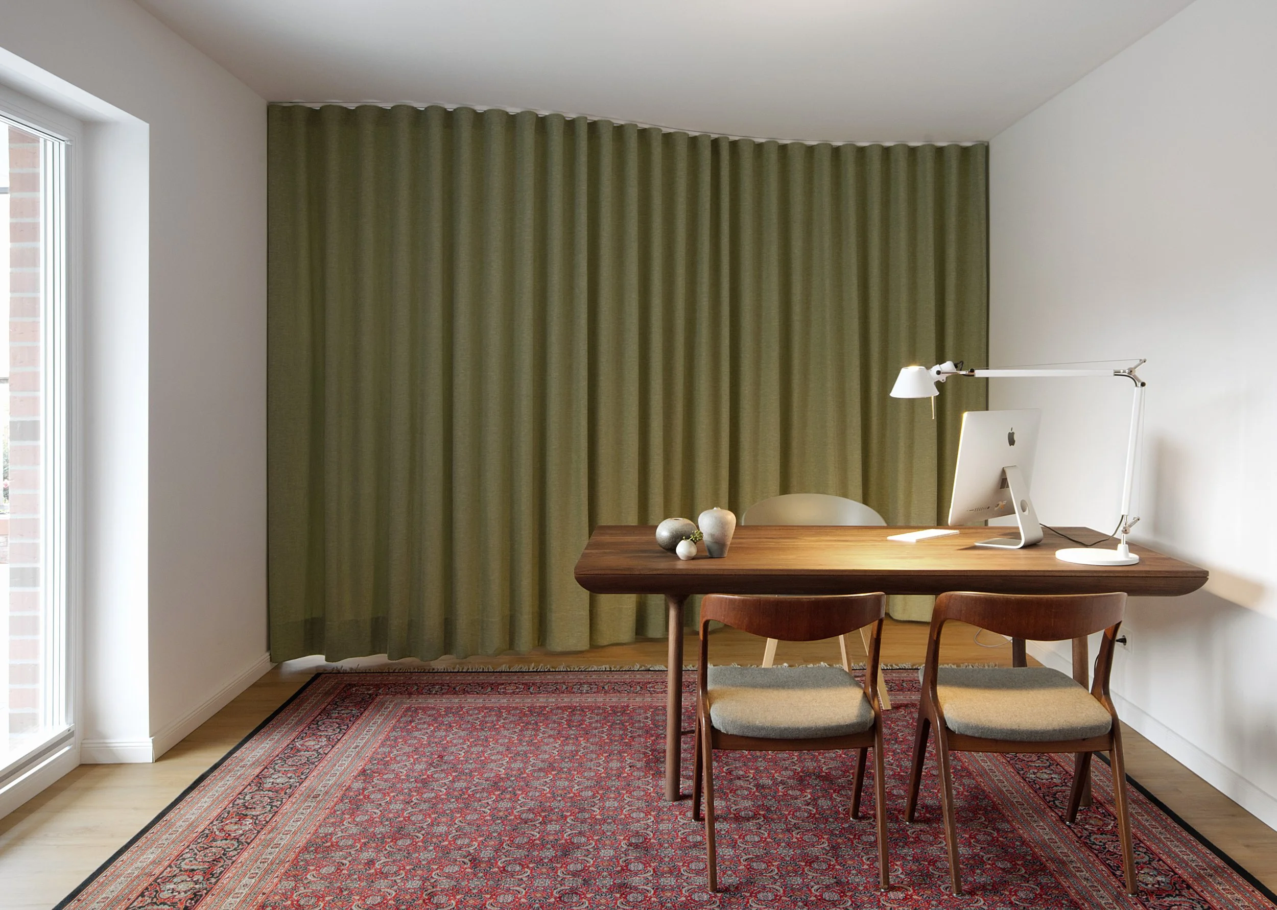 Praxisraum mit grünem Vorhang, Holzmöbeln und Perserteppich