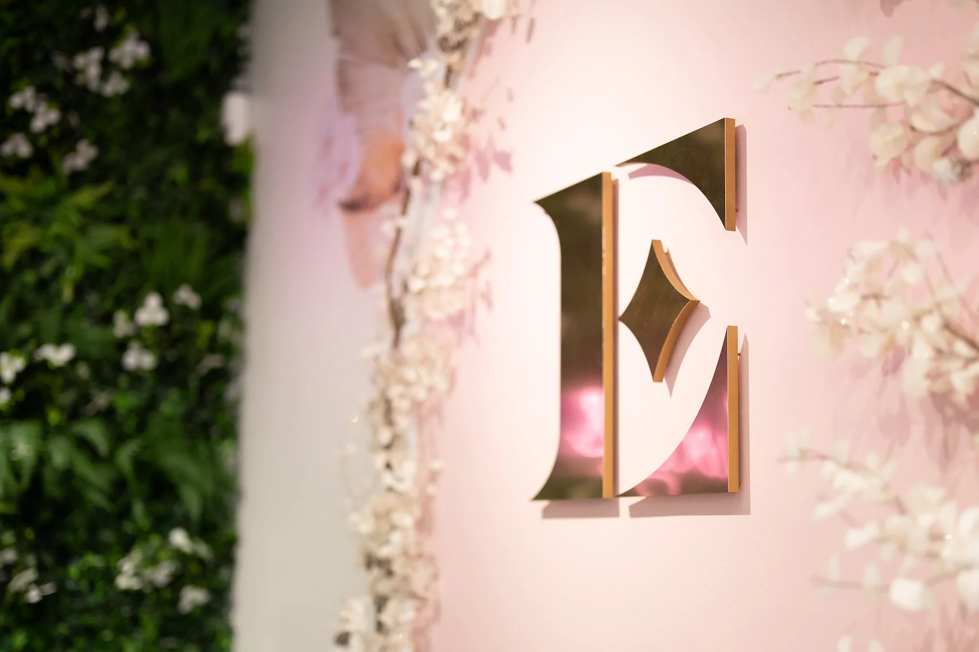 Everglow Jewelry store interior showcasing large 'E' metallic gold sign with florals and greenery wall