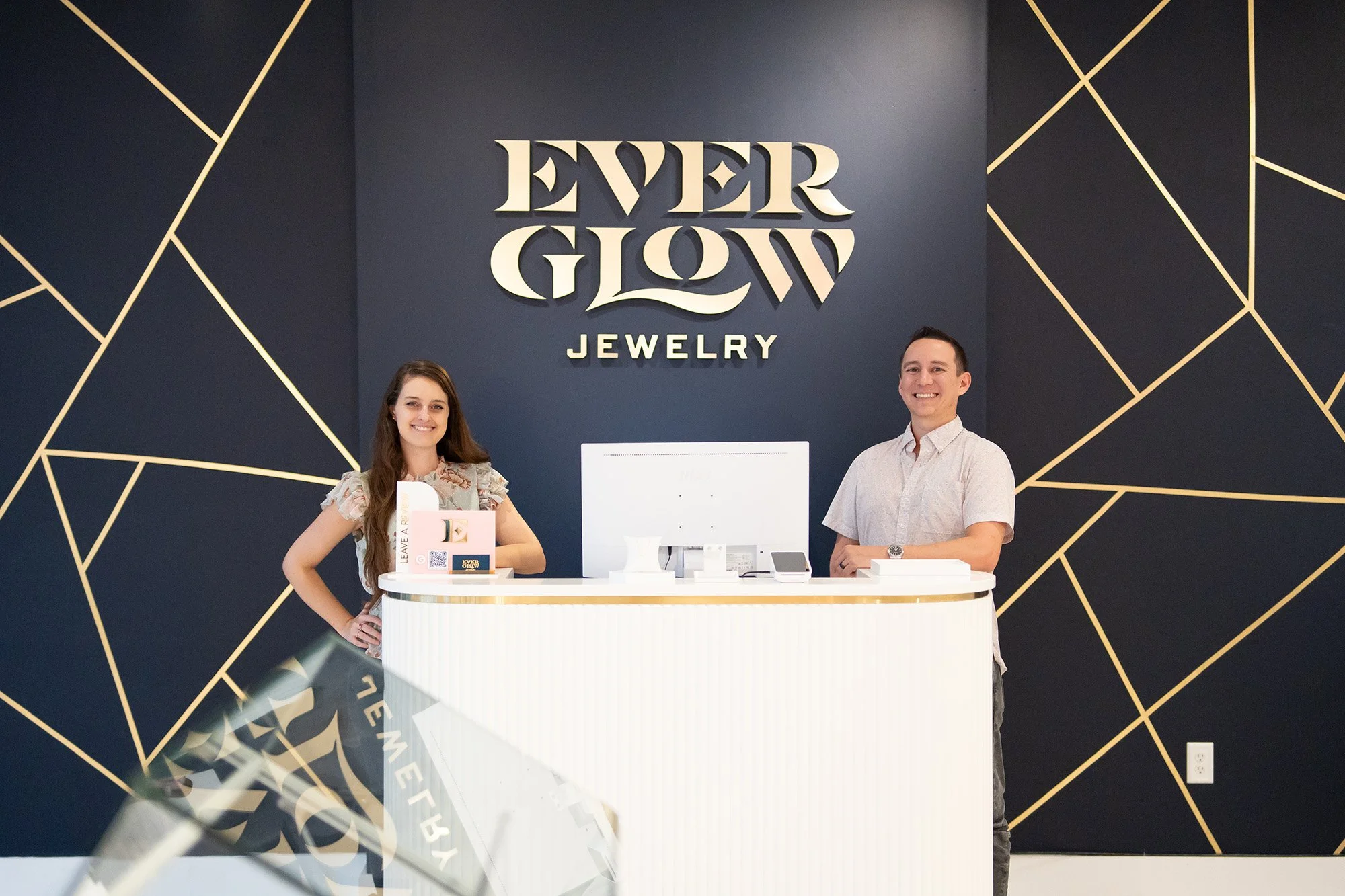 Everglow Jewelry owners pose inside their store facing camera and smiling with Everglow Jewelry signage in the background