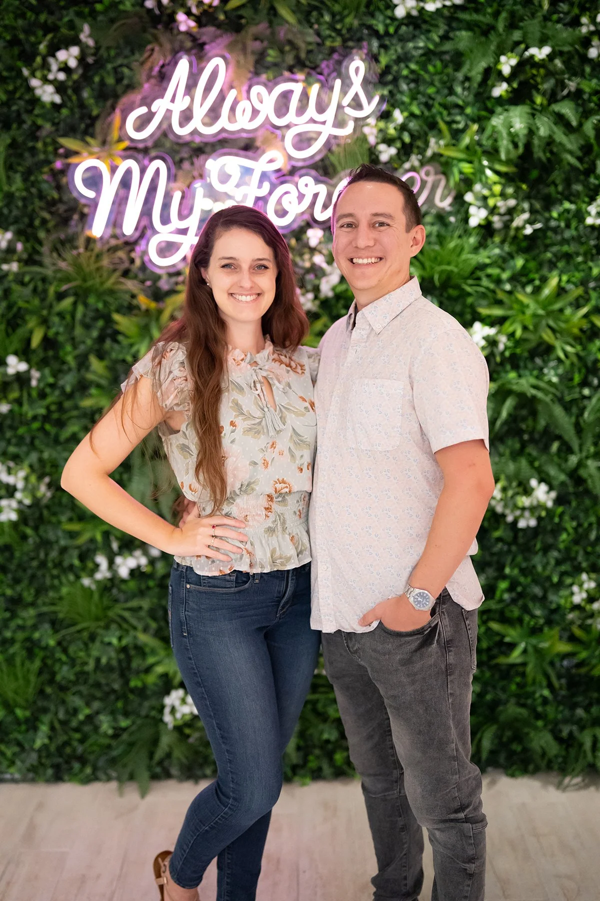 Everglow Jewelry owners pose inside their store in front of a greenery wall