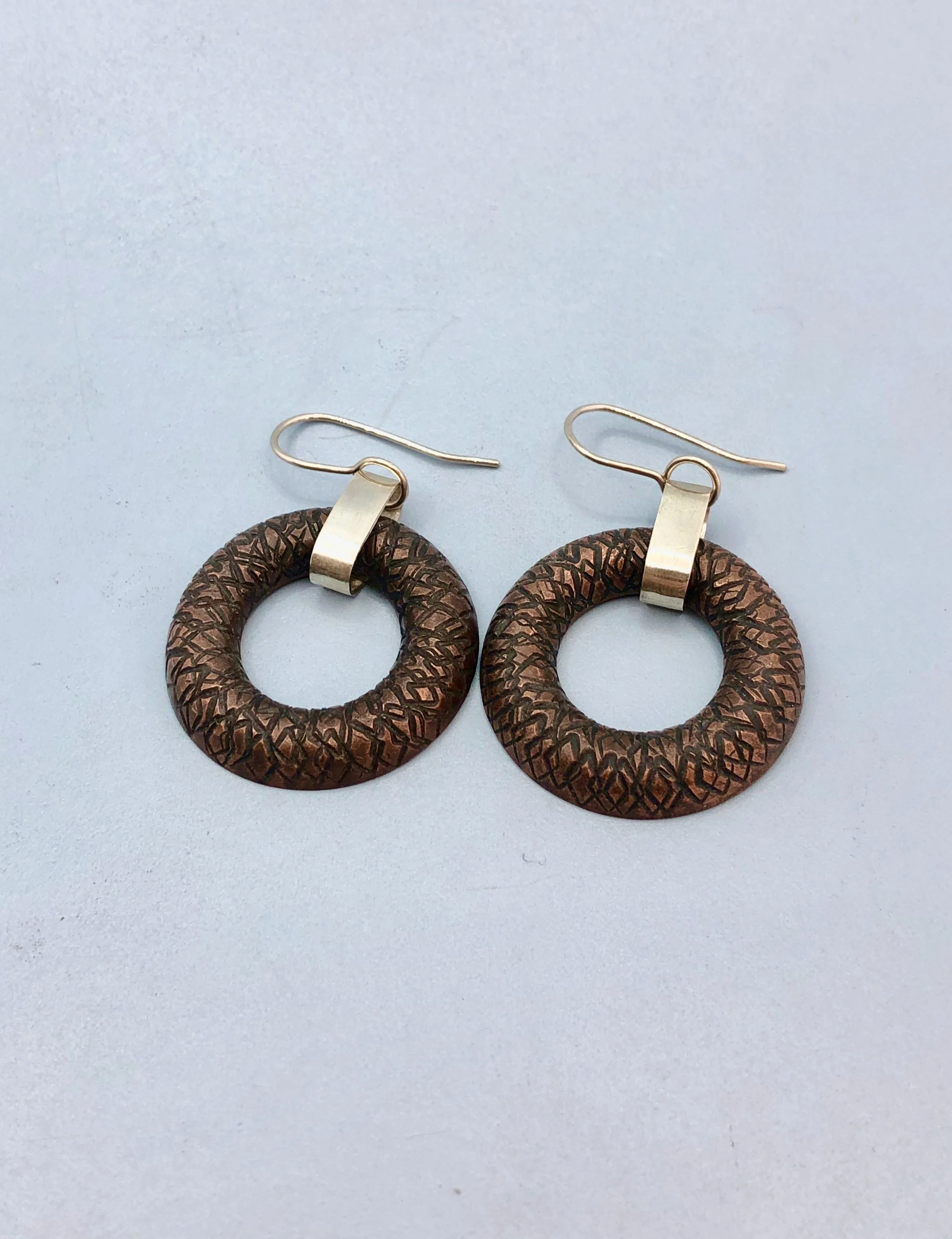 Front view of earring lying down, showing textured copper donut shape and sterling silver chain link and ear hook