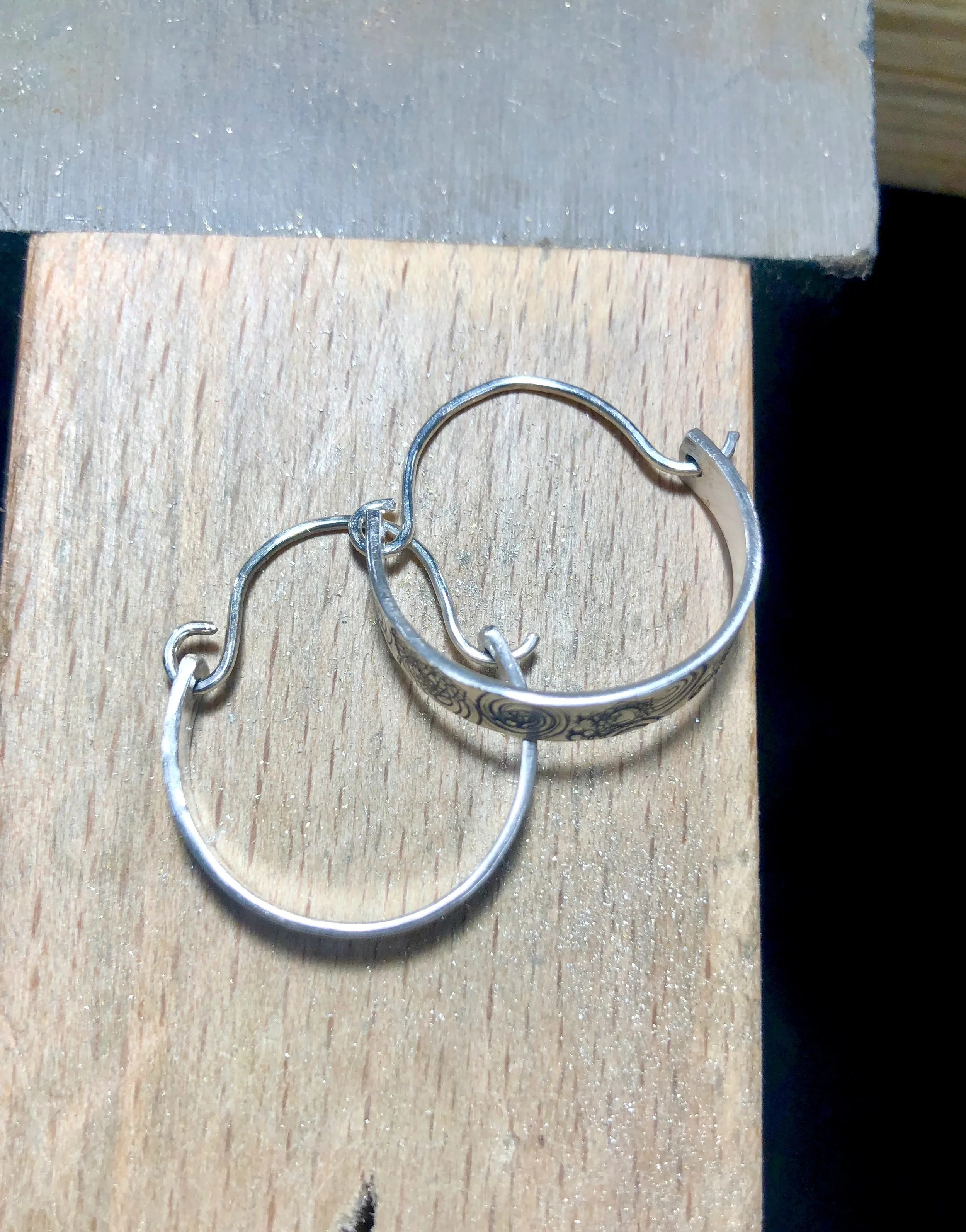 Sterling silver textured half hoop earrings with silver half hoop hook, sitting on a bench peg of a jewellers workbench