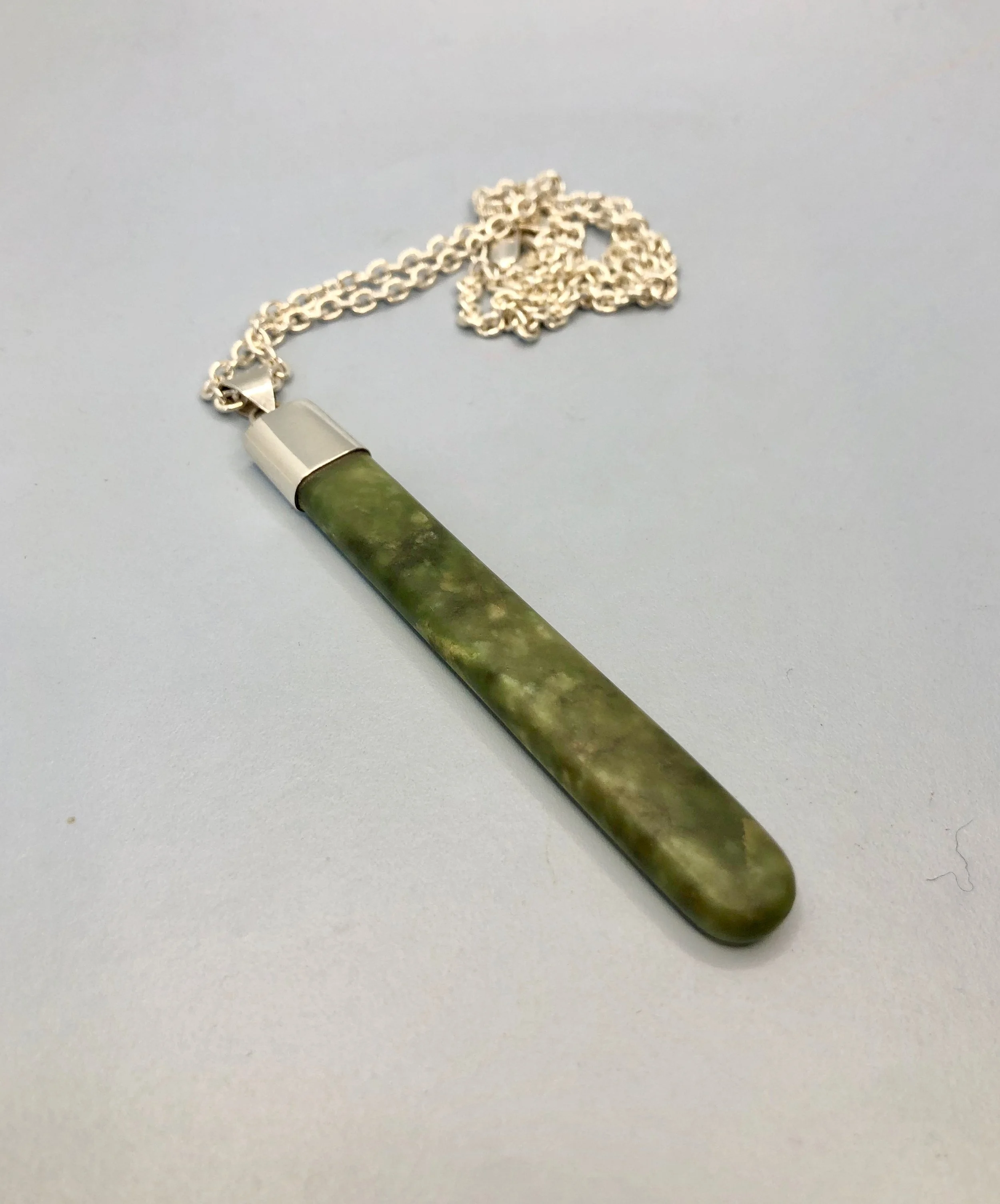 Pounamu pendant shown lying down from side view, reverse side.