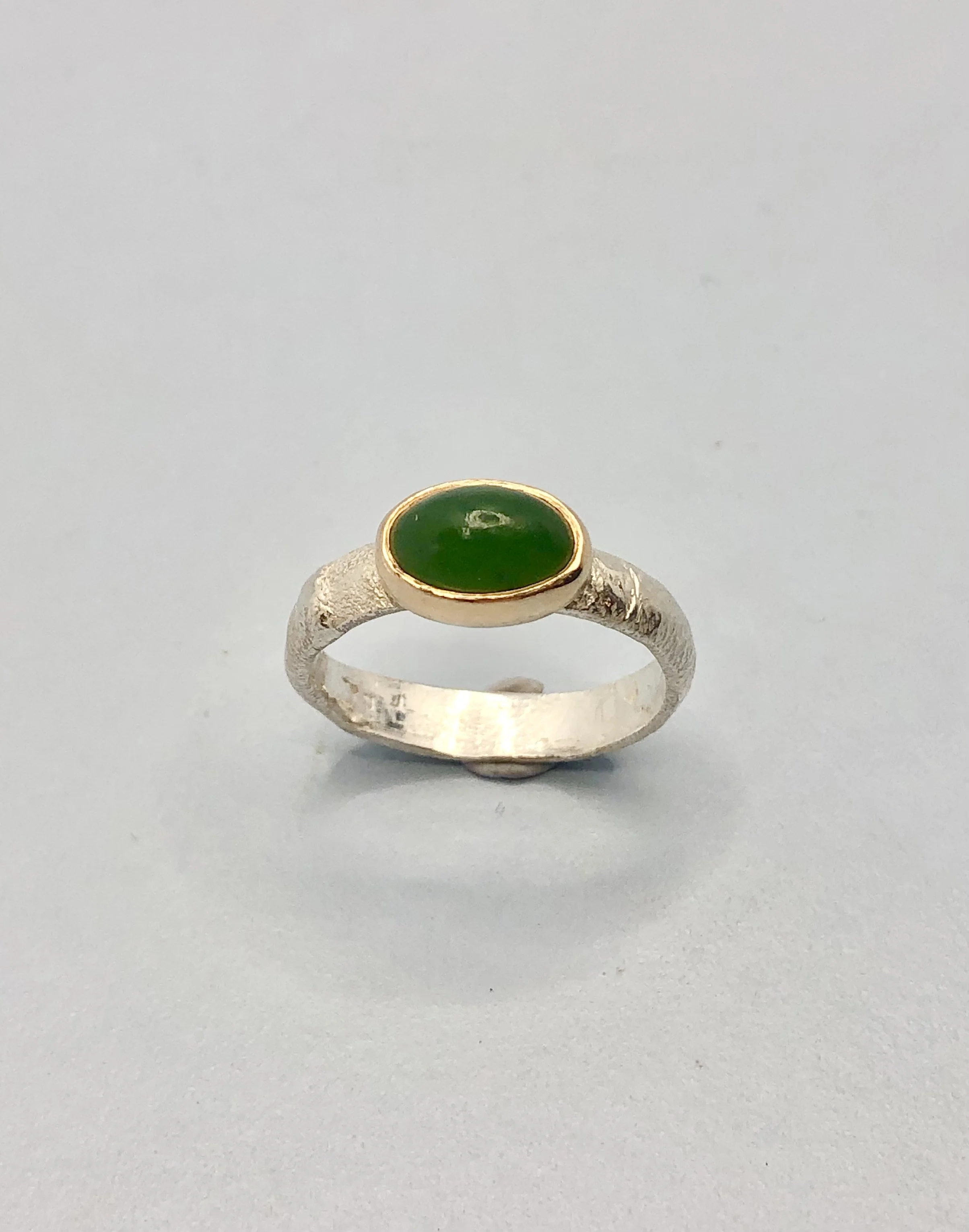 Top-down view of oval pounamu stone in yellow gold setting on textured silver ring