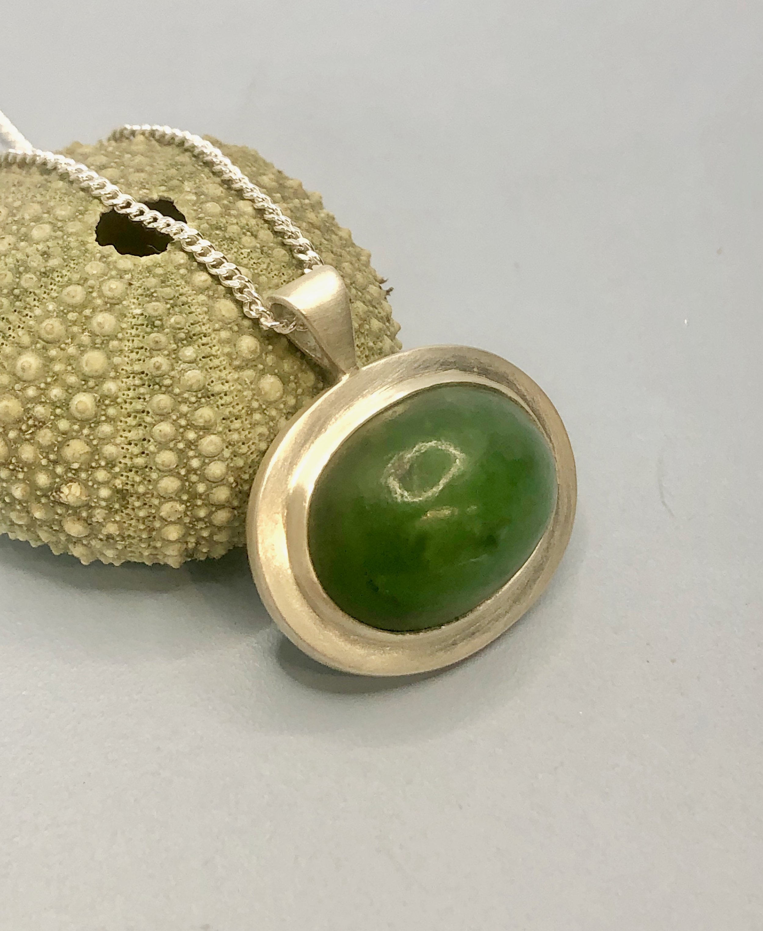 Oval dome pounamu pendant propped up against kina shell on side to show depth