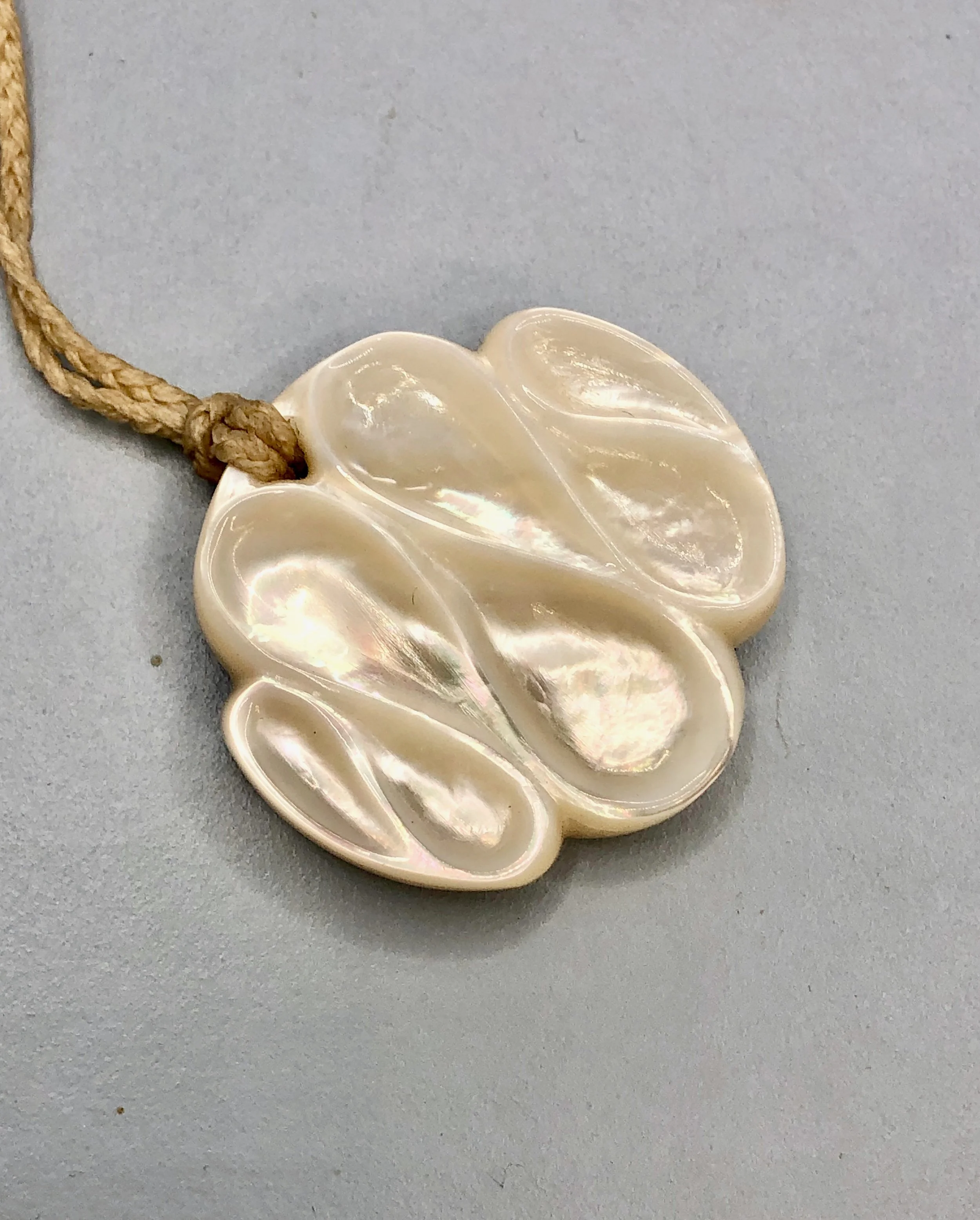 Angled view of Australian mother of pearl shell pendant with a carved infinity shapes
