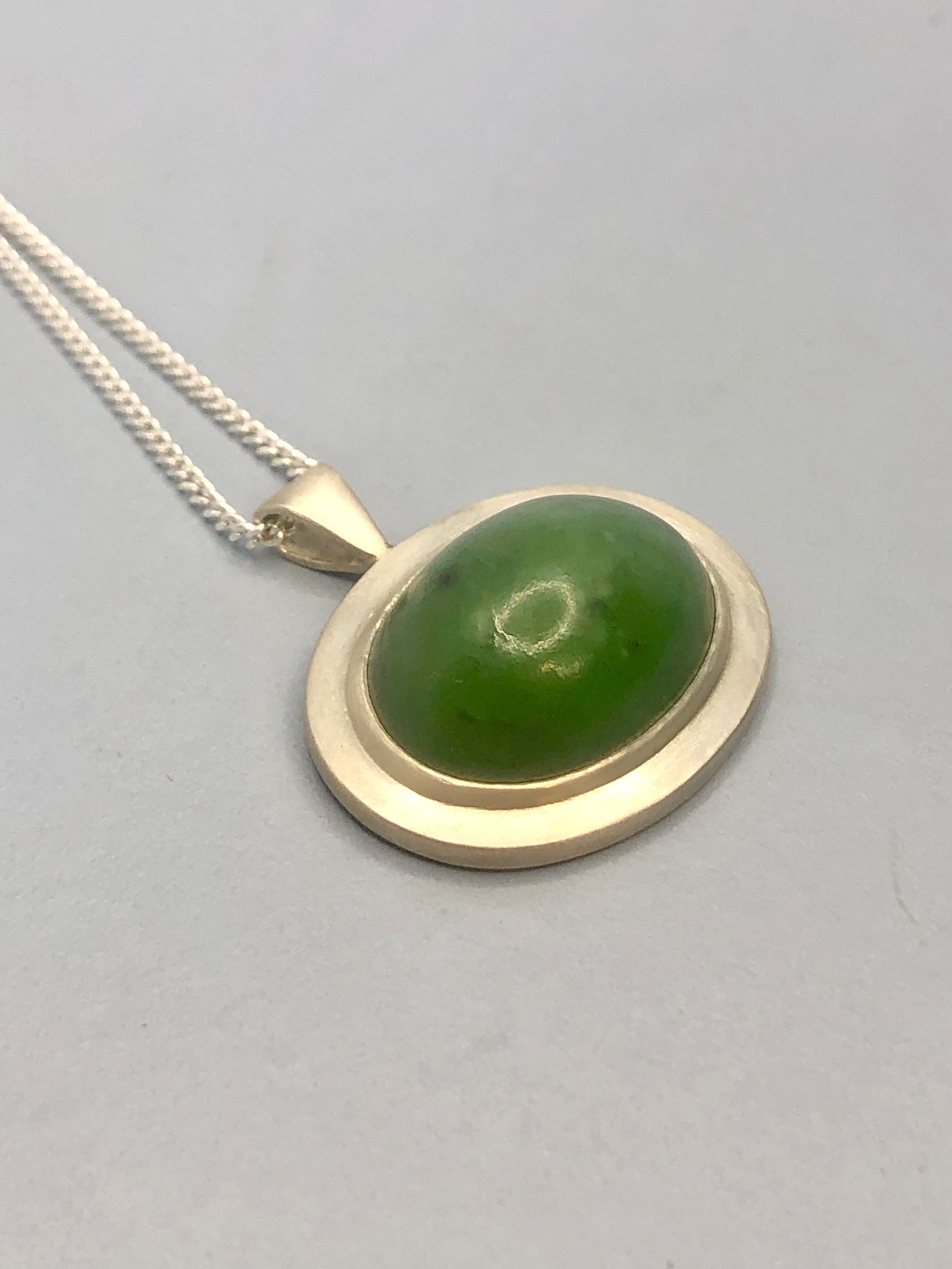 Side view of greenstone pendant lying down.