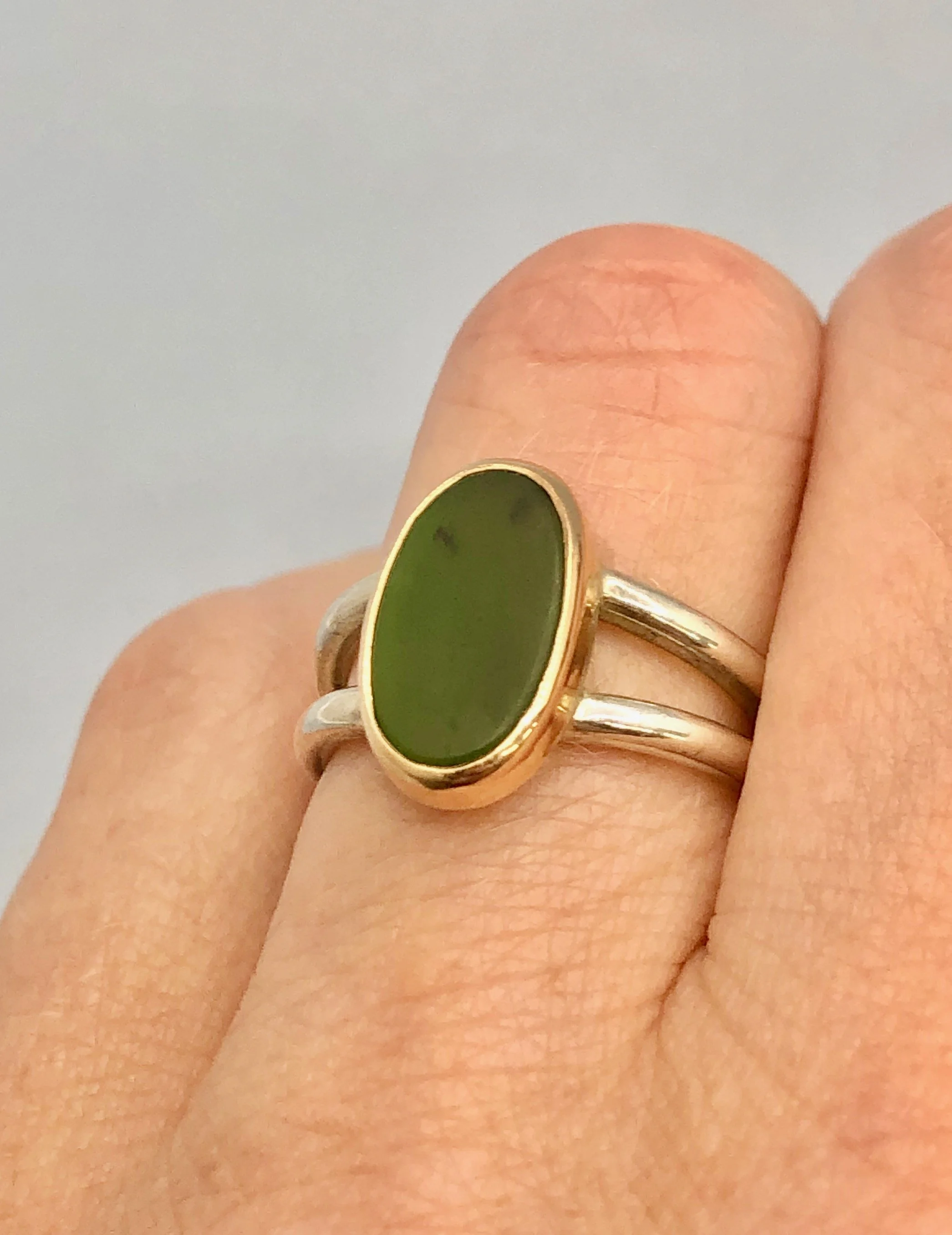 Pounamu split-shank ring worn on finger, showing gold setting and silver band detail