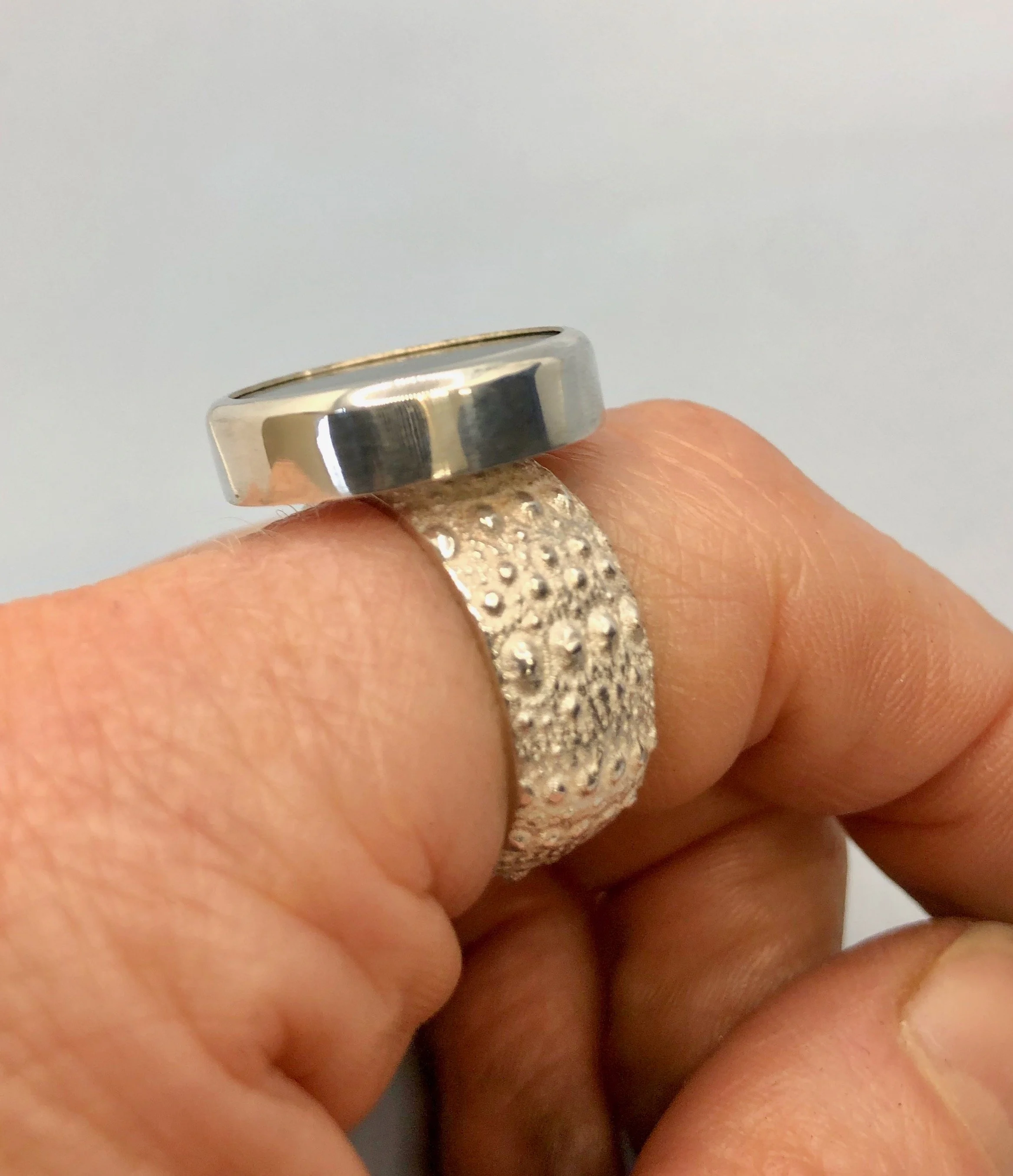 NZ Pounamu disc ring set on Kina textured band shown worn on finger from side view.