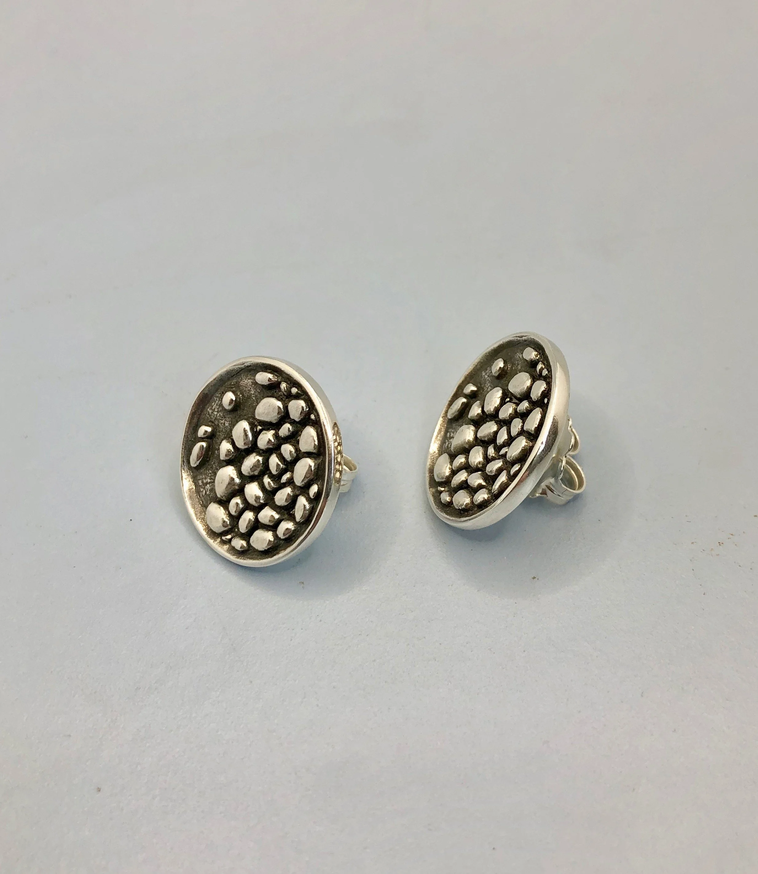Wax carved and cast in sterling silver stony river textured stud earrings shown on side profile.